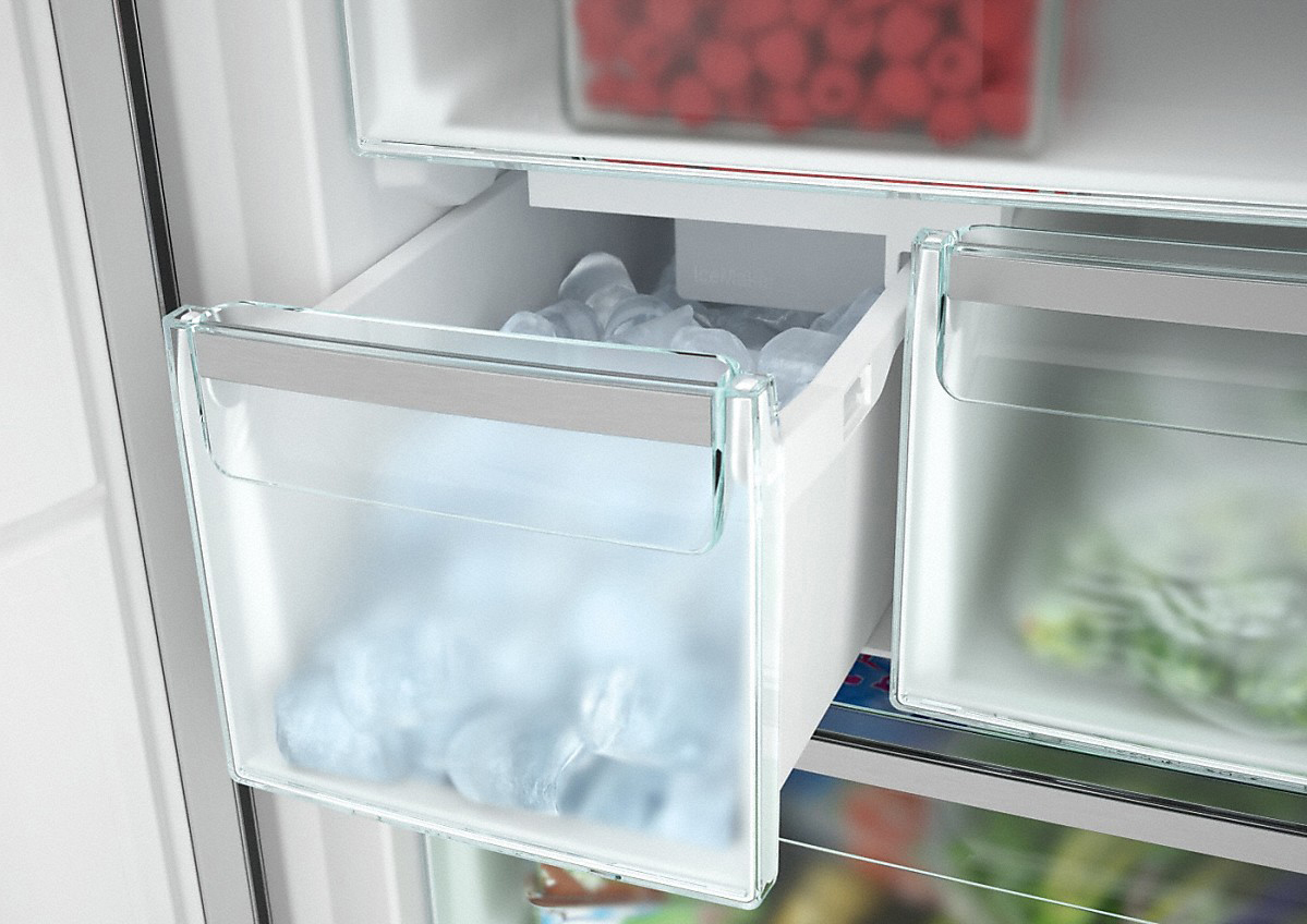Kühlschrankinnenraum: Eiswürfel in einer transparenten Schublade, darüber ein roter Behälter.