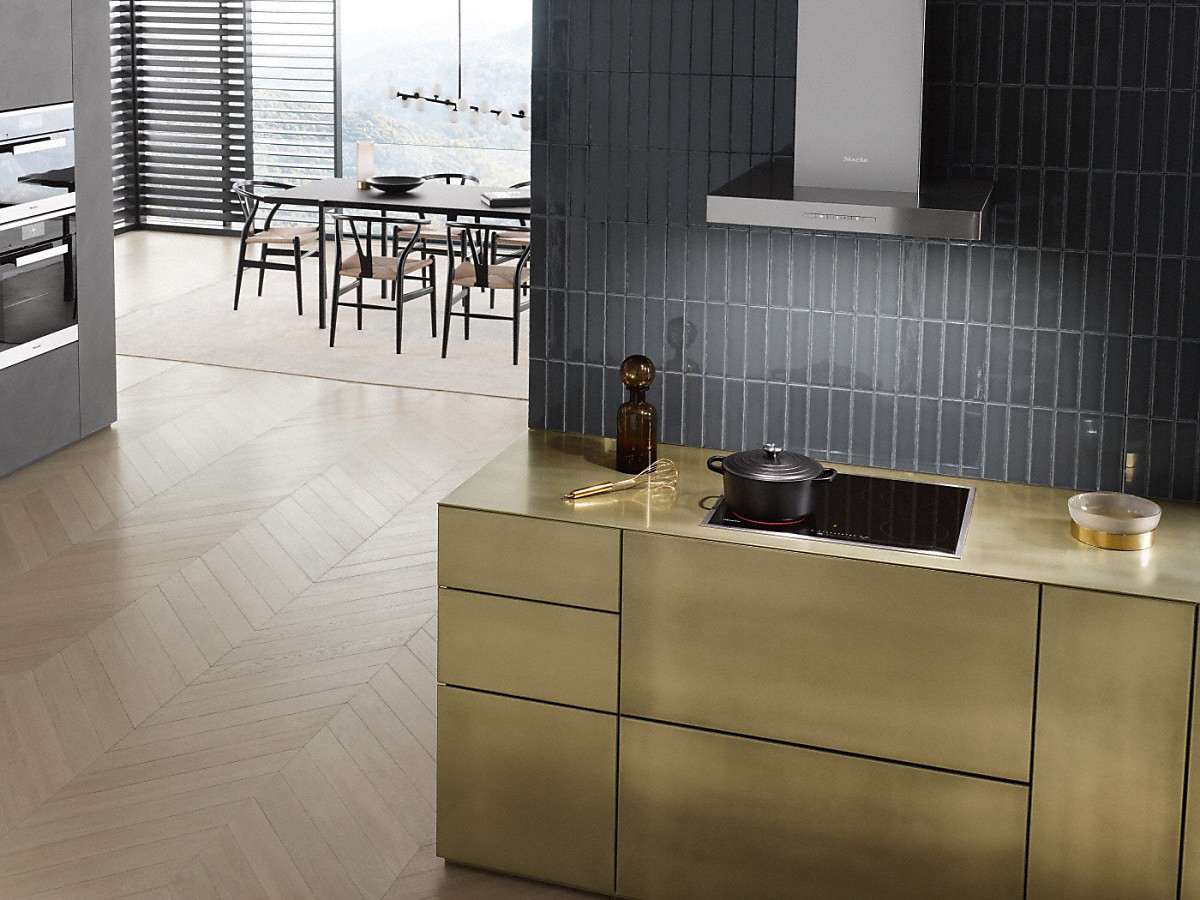Moderne Küche mit Goldschränken, schwarzem Kochfeld und Essbereich.