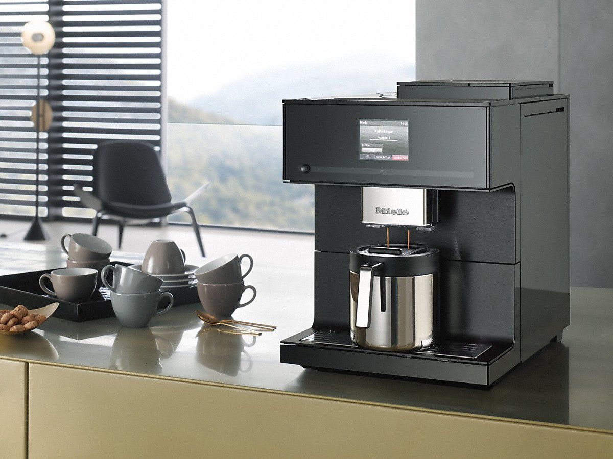 Eine schwarze Kaffeemaschine brüht Kaffee in eine Metallkaraffe, auf einer goldenen Theke.