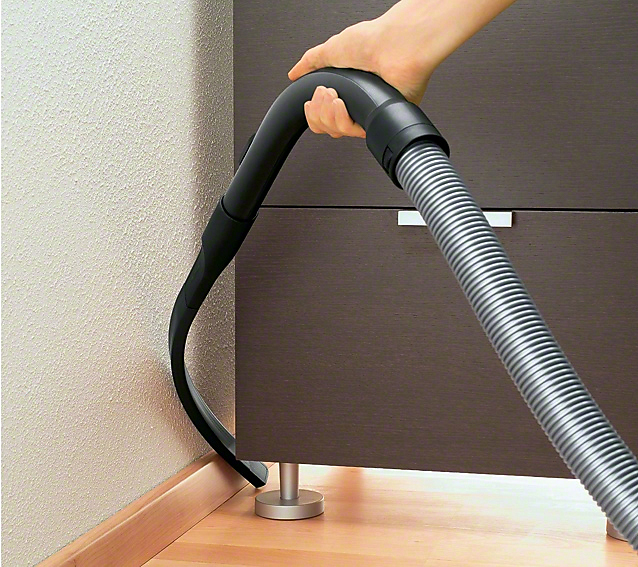 Eine Hand staubsaugt einen Bereich in der Nähe eines Schranks.