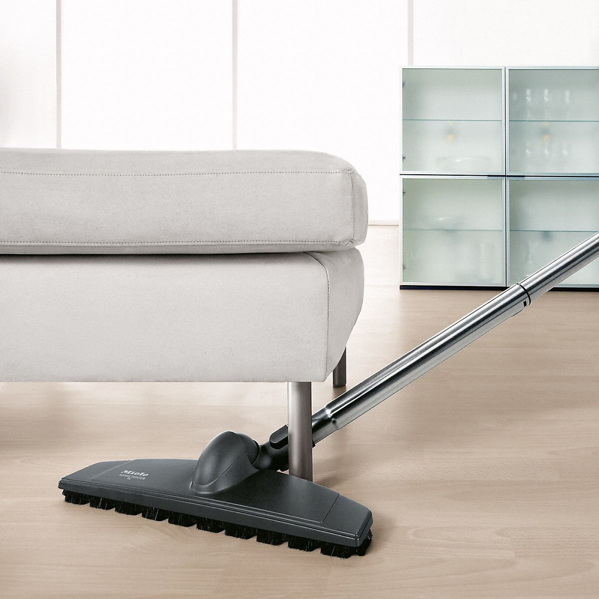 Ein Staubsaugerkopf auf einem Holzboden neben einer Couch.