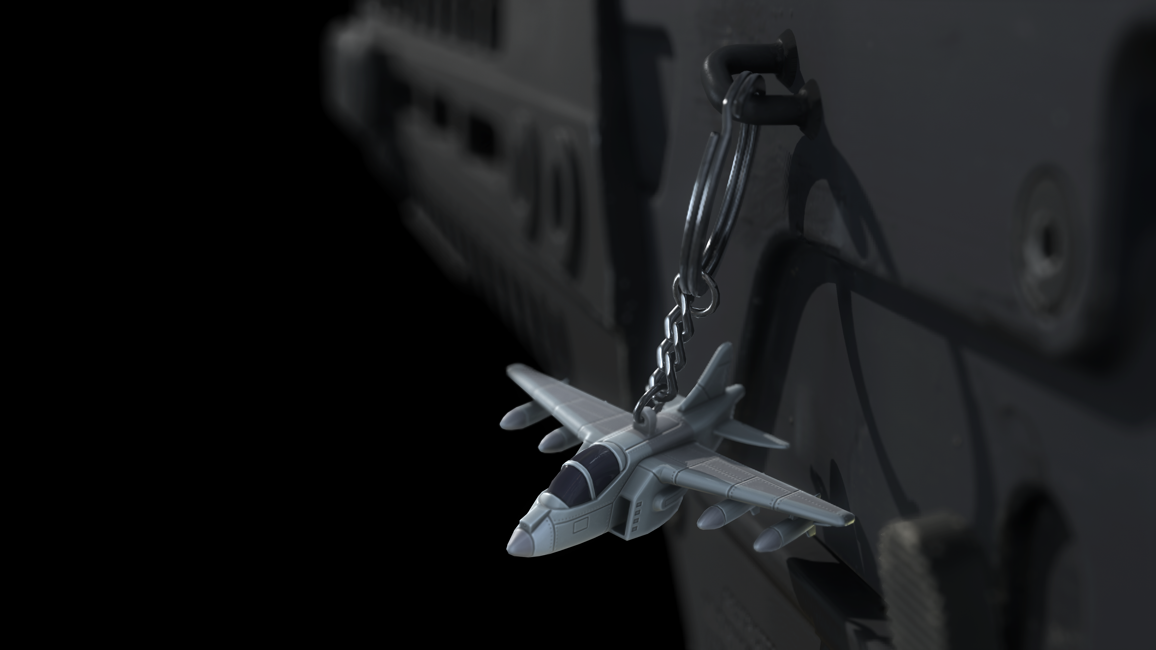 Un pequeño llavero de avión colgando de un objeto oscuro, posiblemente un arma. Fondo negro.