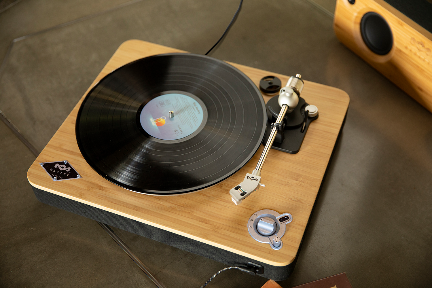 Platenspeler met zwarte vinylplaat op houten oppervlak. Een luidspreker op de achtergrond.
