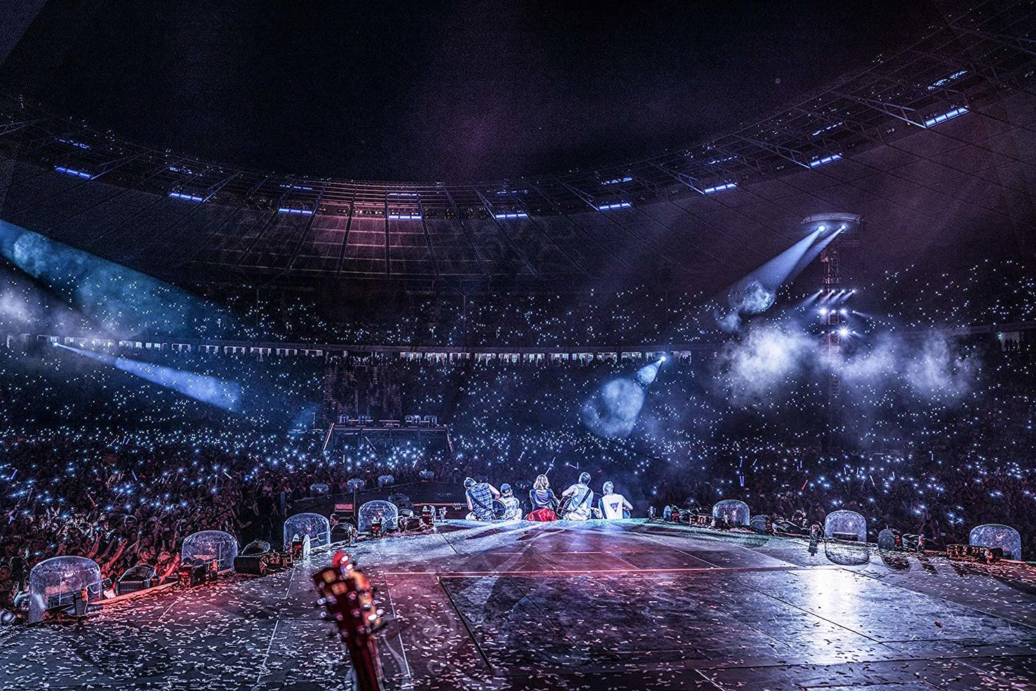 Konzertbühne mit Band und Publikum, das Lichter in einer großen Halle hochhält.