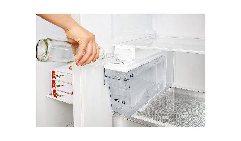 Una mano vierte agua en un recipiente de agua transparente del refrigerador. Hay cajas de pizza cerca.