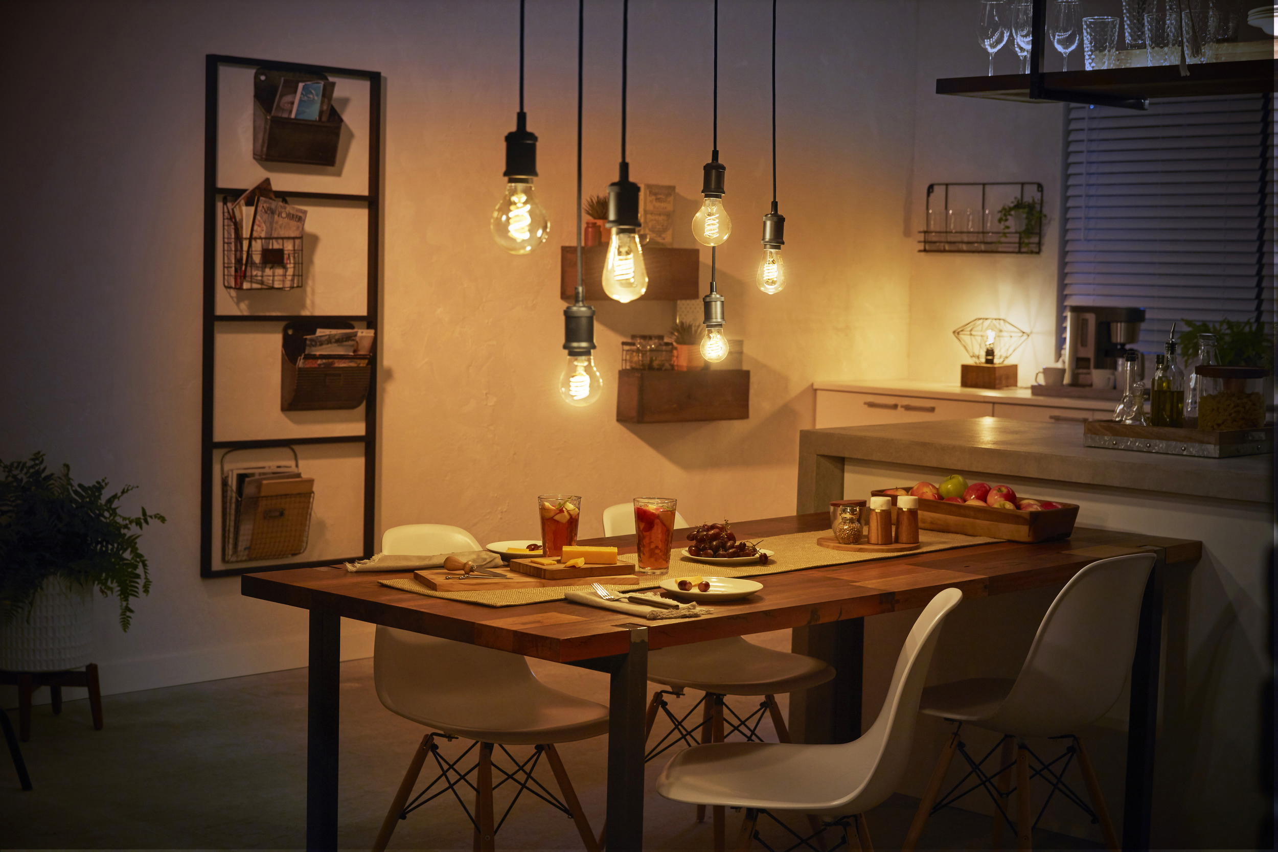 Ein Esszimmer mit Pendelleuchten, einem Holztisch, der zum Abendessen gedeckt ist, und warmer Beleuchtung.