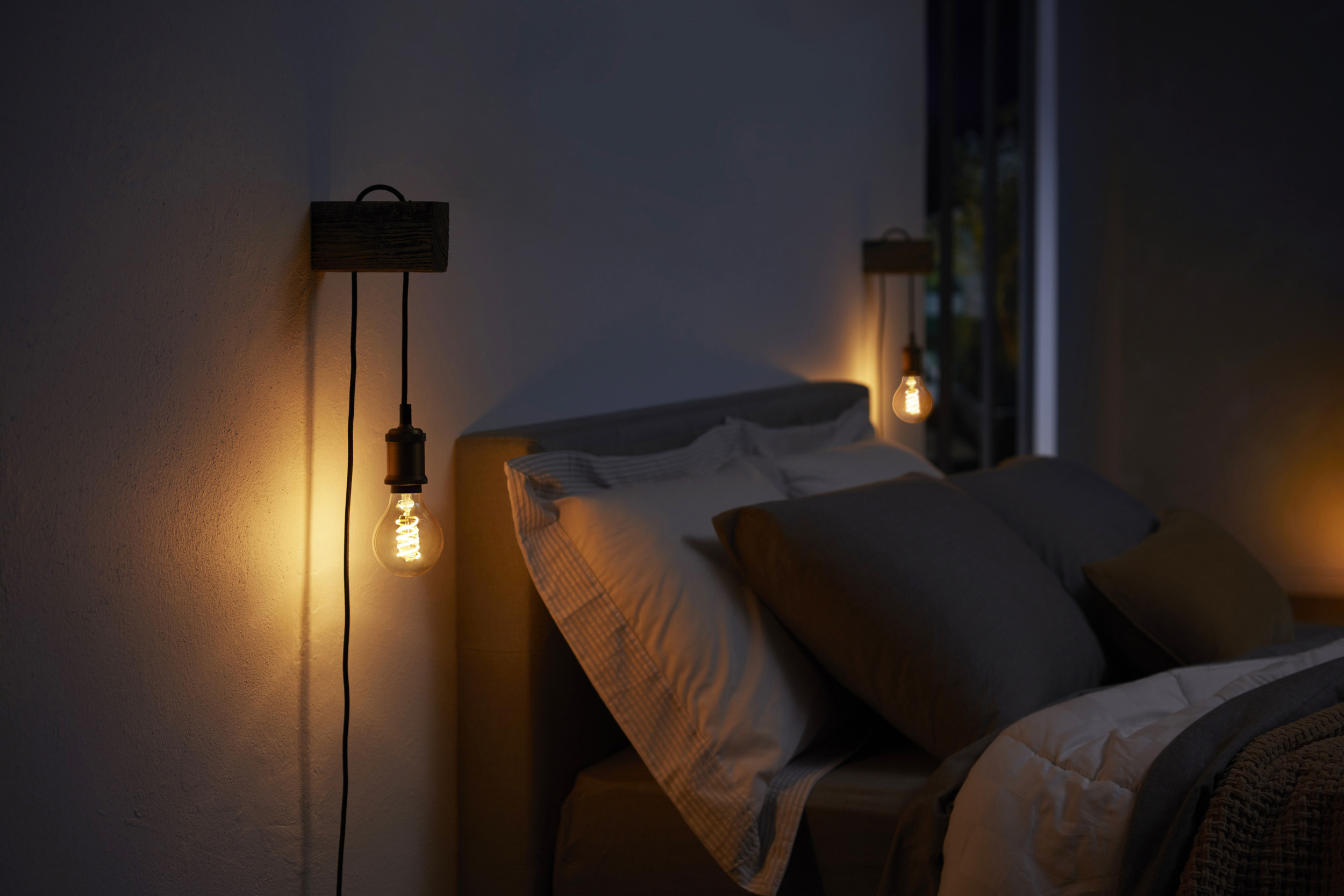 Zwei Glühbirnen im Edison-Stil beleuchten ein Schlafzimmer und werfen warmes Licht.