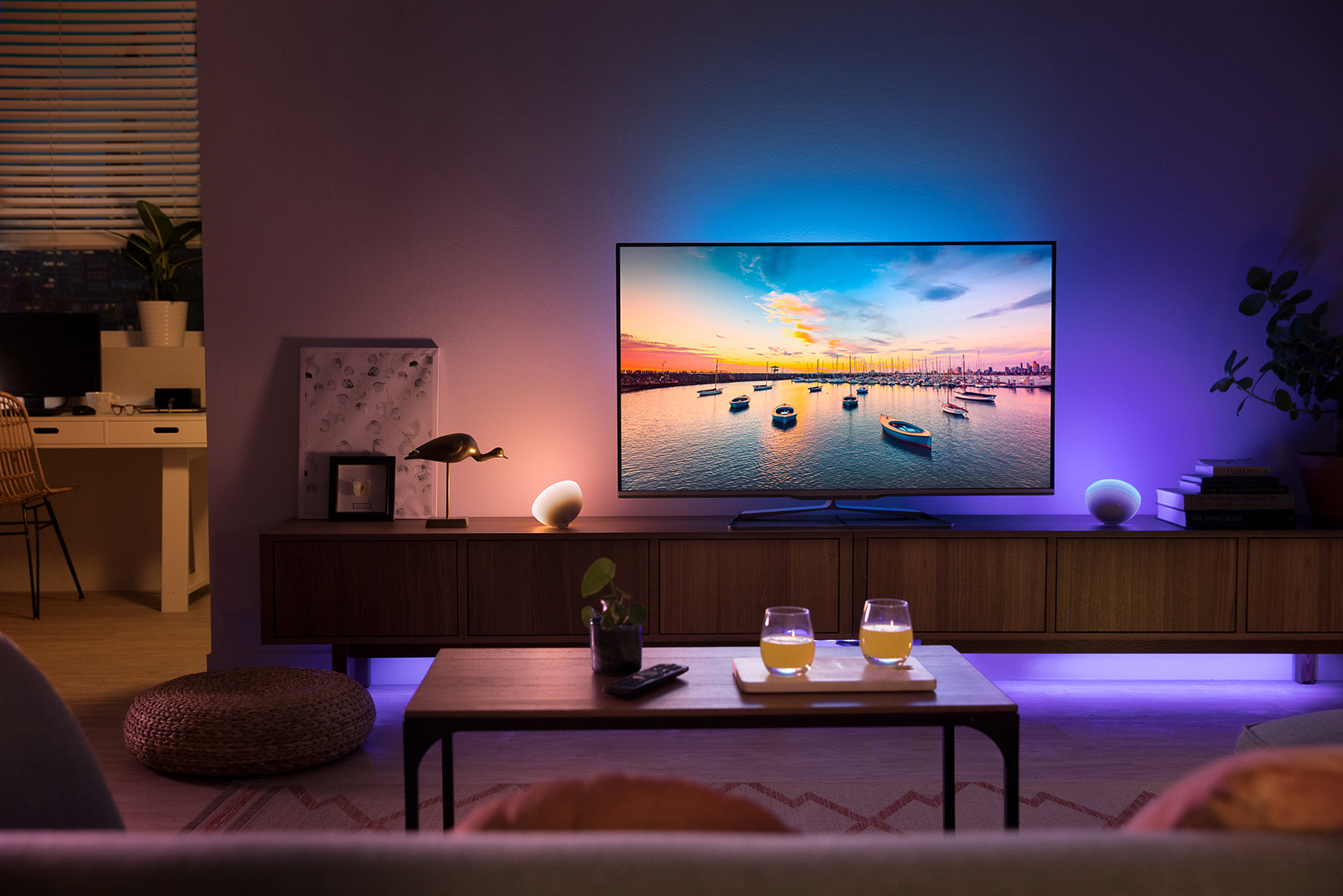Wohnzimmer mit Fernseher, der eine Hafenszene zeigt. Zwei Gläser auf dem Tisch, Seitenlichter und Hintergrundbeleuchtung.