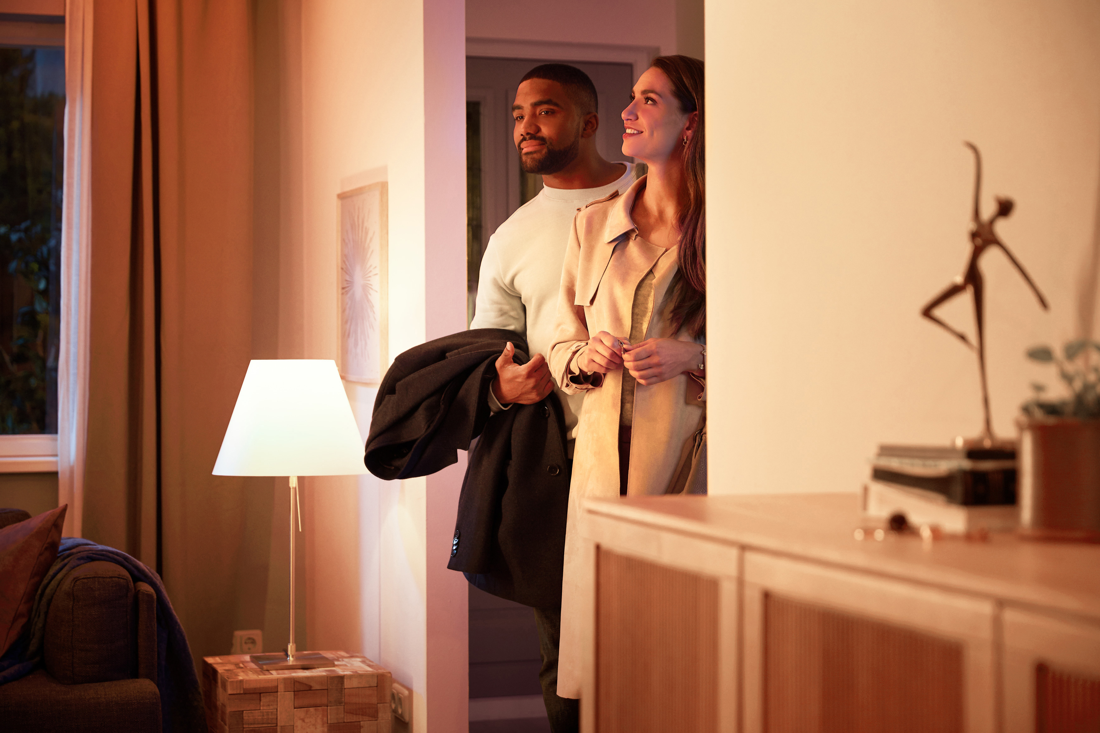 Ein Paar steht in einem hell beleuchteten Türrahmen und schaut weg. Links ist eine Lampe.