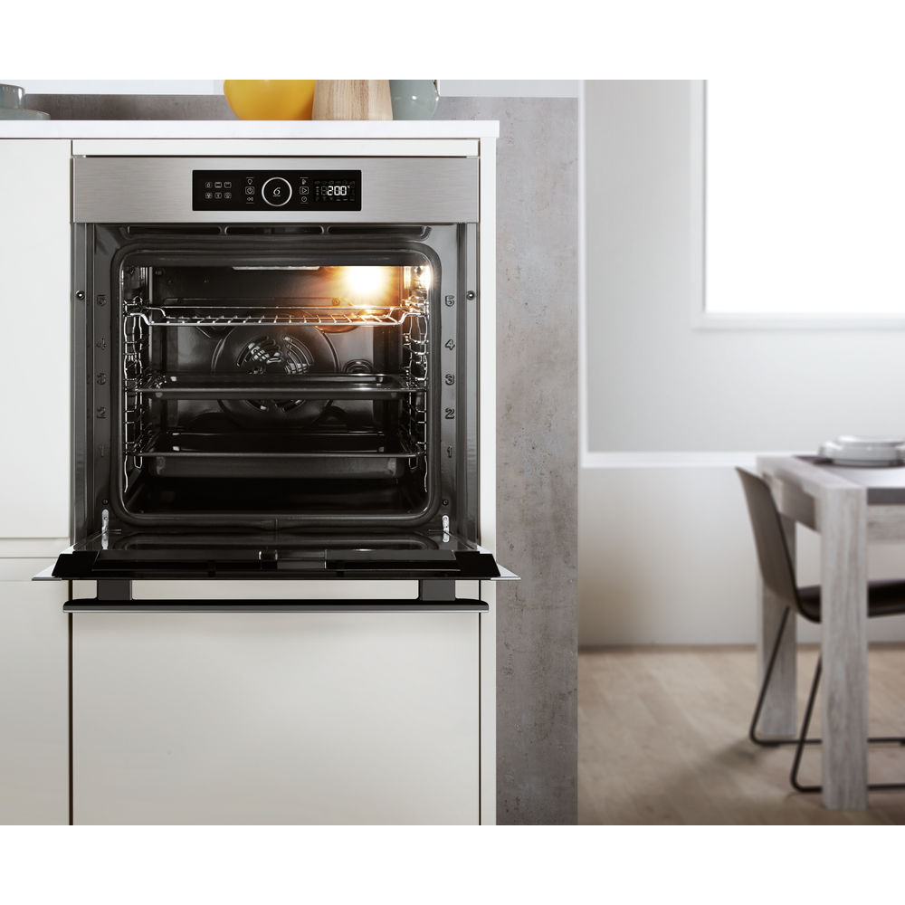 Open oven met binnenrekken, digitale display toont tijd. Witte kasten en een tafel op de achtergrond.