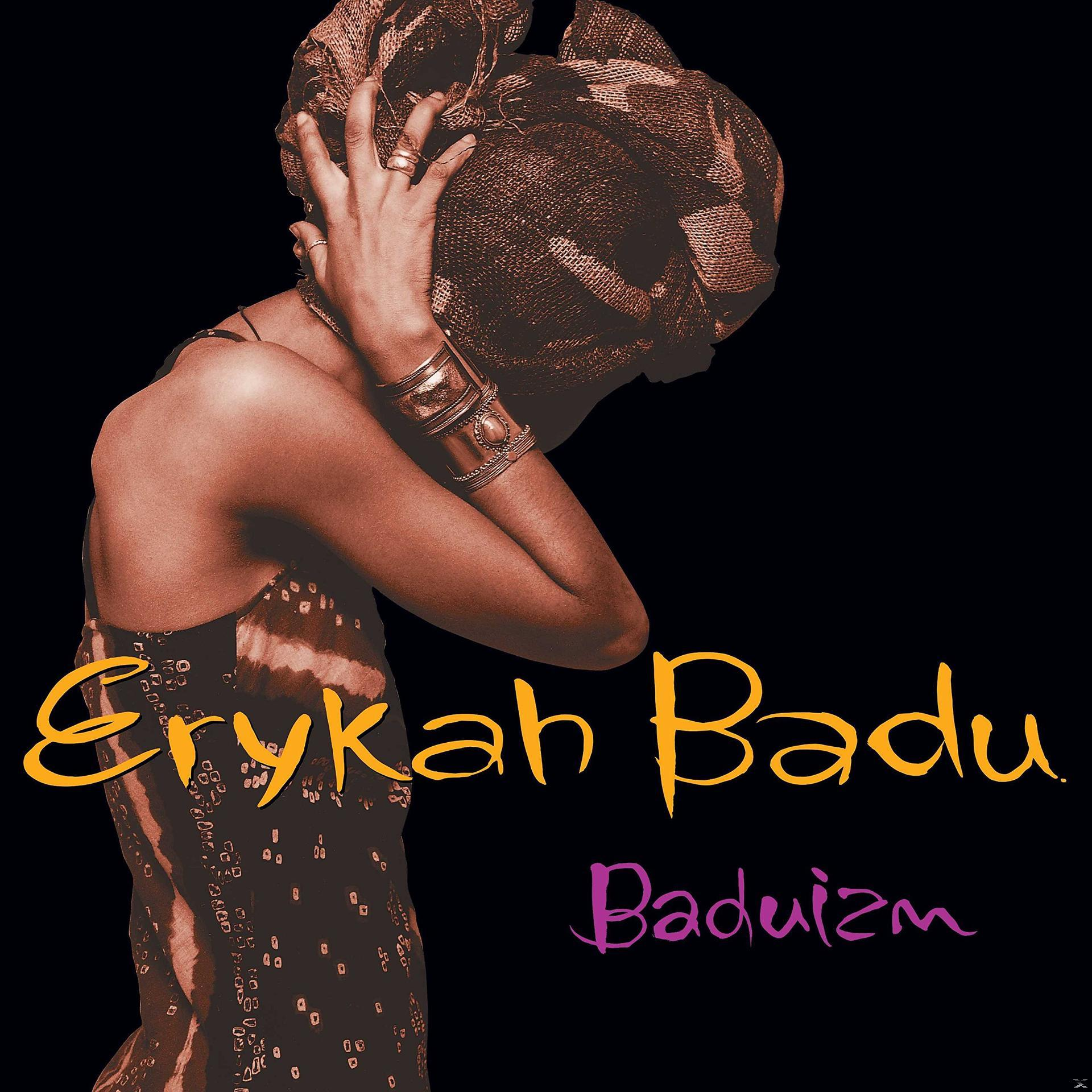 A woman in a headwrap and jewelry covers her face against a black background.