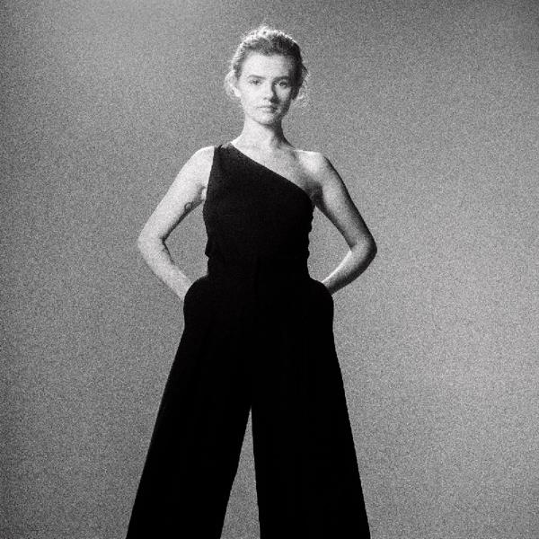 Schwarz-Weiß-Foto einer Frau in einem schwarzen Overall, Hände in den Taschen.