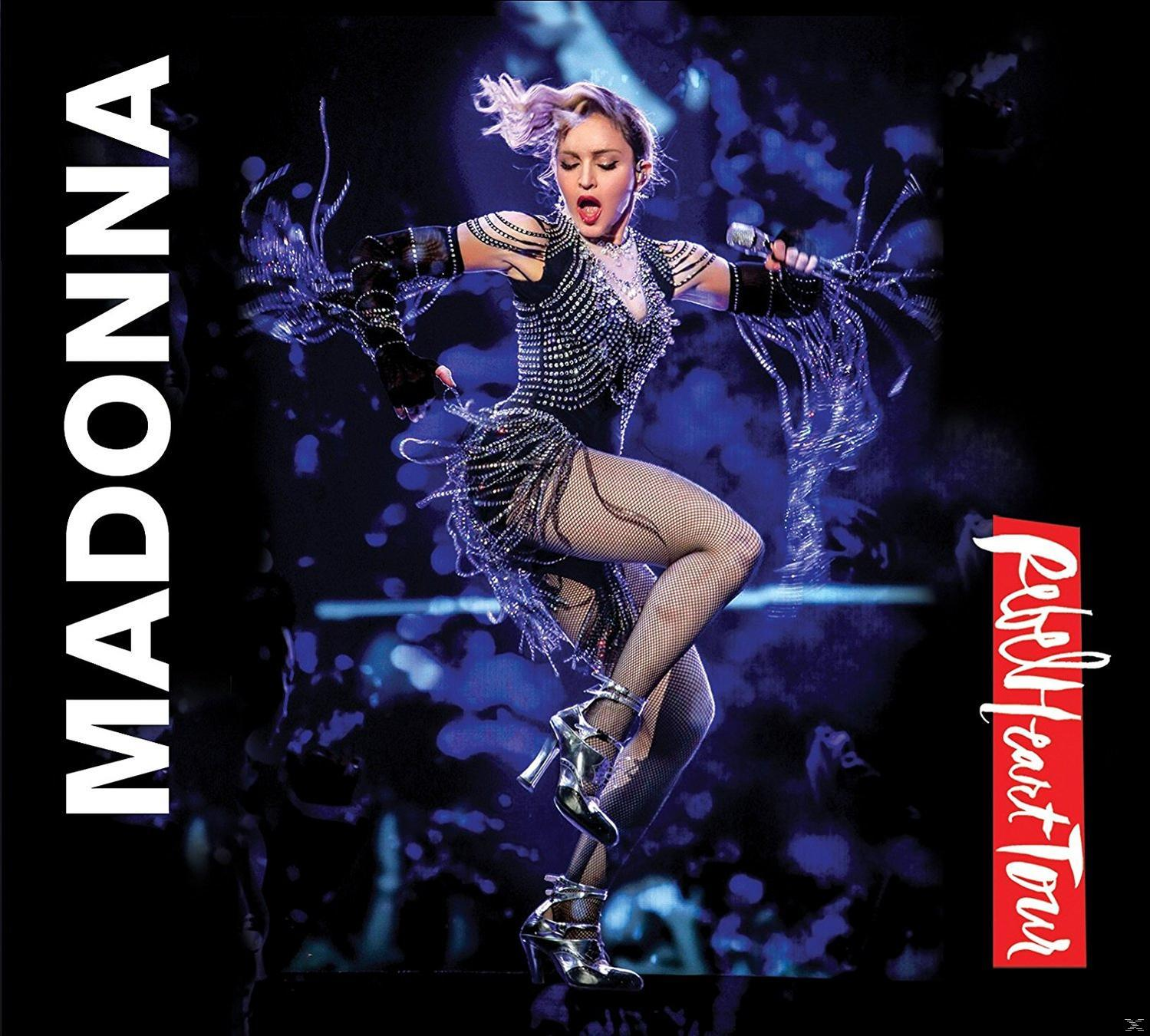 Madonna op het podium, draagt een met juwelen bezette outfit en visnetkousen. De achtergrond is donker met de tournaam.