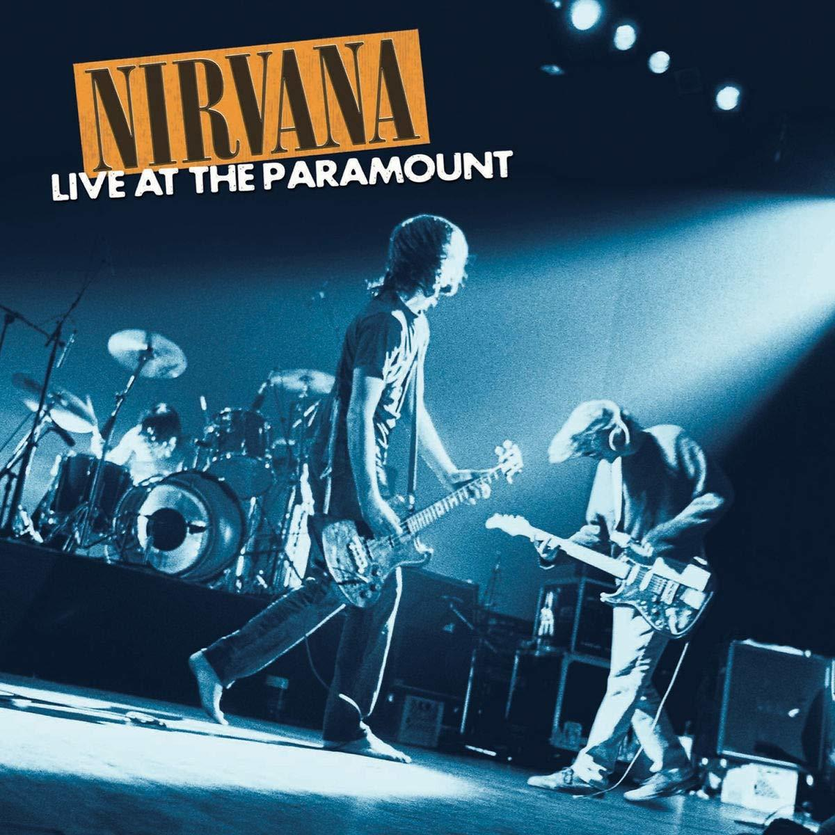 Performance live de Nirvana. Deux guitaristes sur scène, batterie en arrière-plan, éclairage bleu.