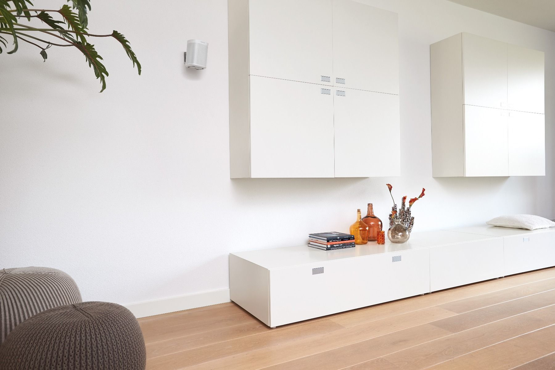 Ein modernes Wohnzimmer mit weißen Möbeln, Holzboden und Wandlautsprecher.
