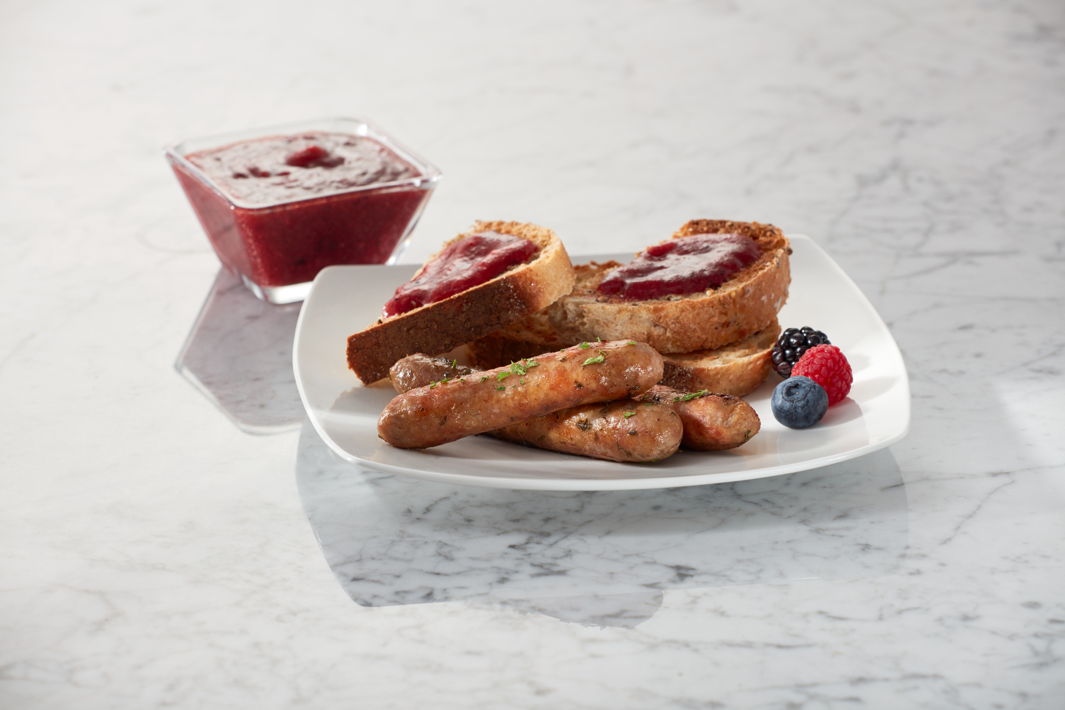 Ein Teller mit Toast mit Marmelade, Würstchen und Beeren, mit einer Marmeladenschüssel.