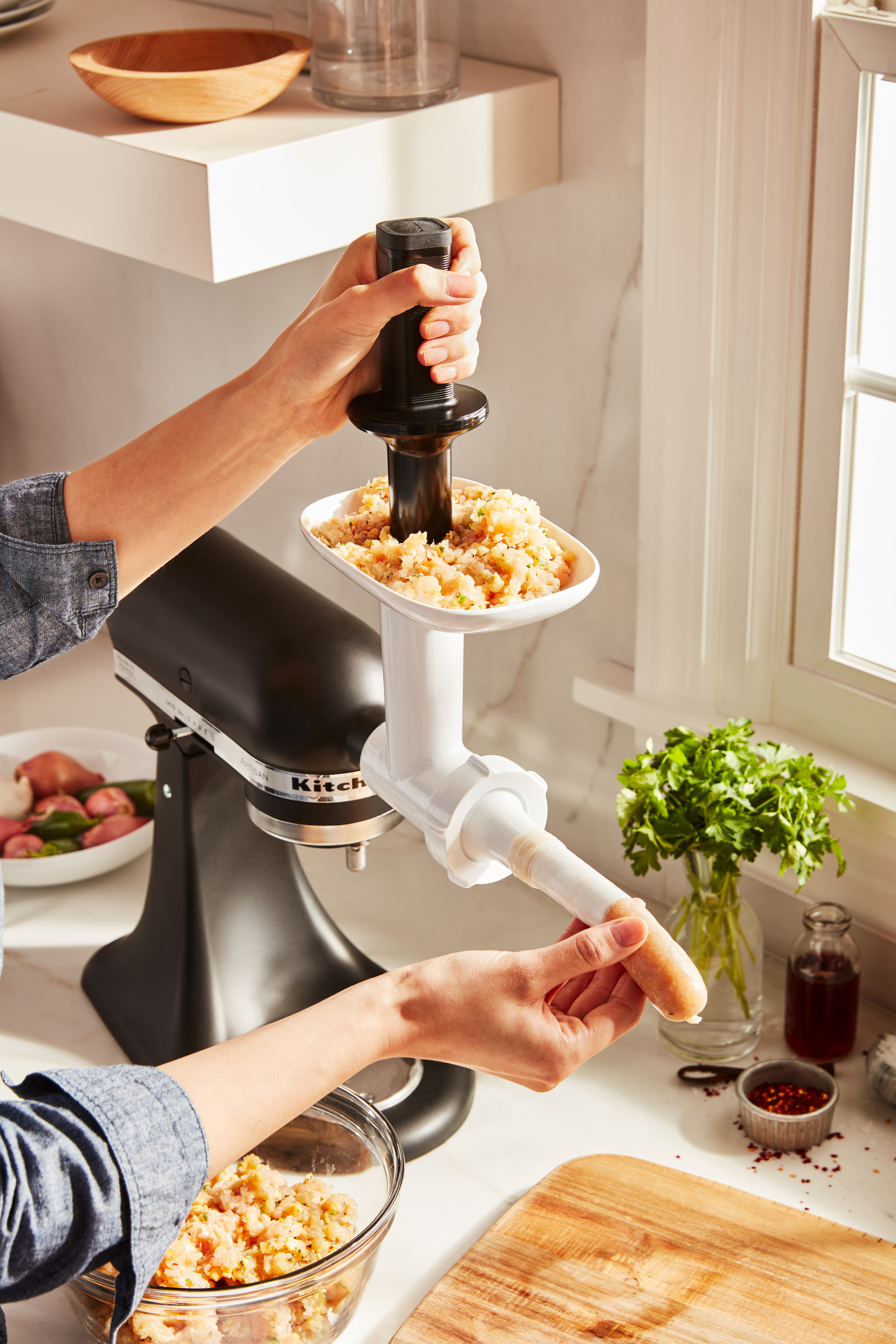 Eine Person verwendet einen KitchenAid Mixer-Aufsatz, um Wurst herzustellen, mit Zutaten im Bild.