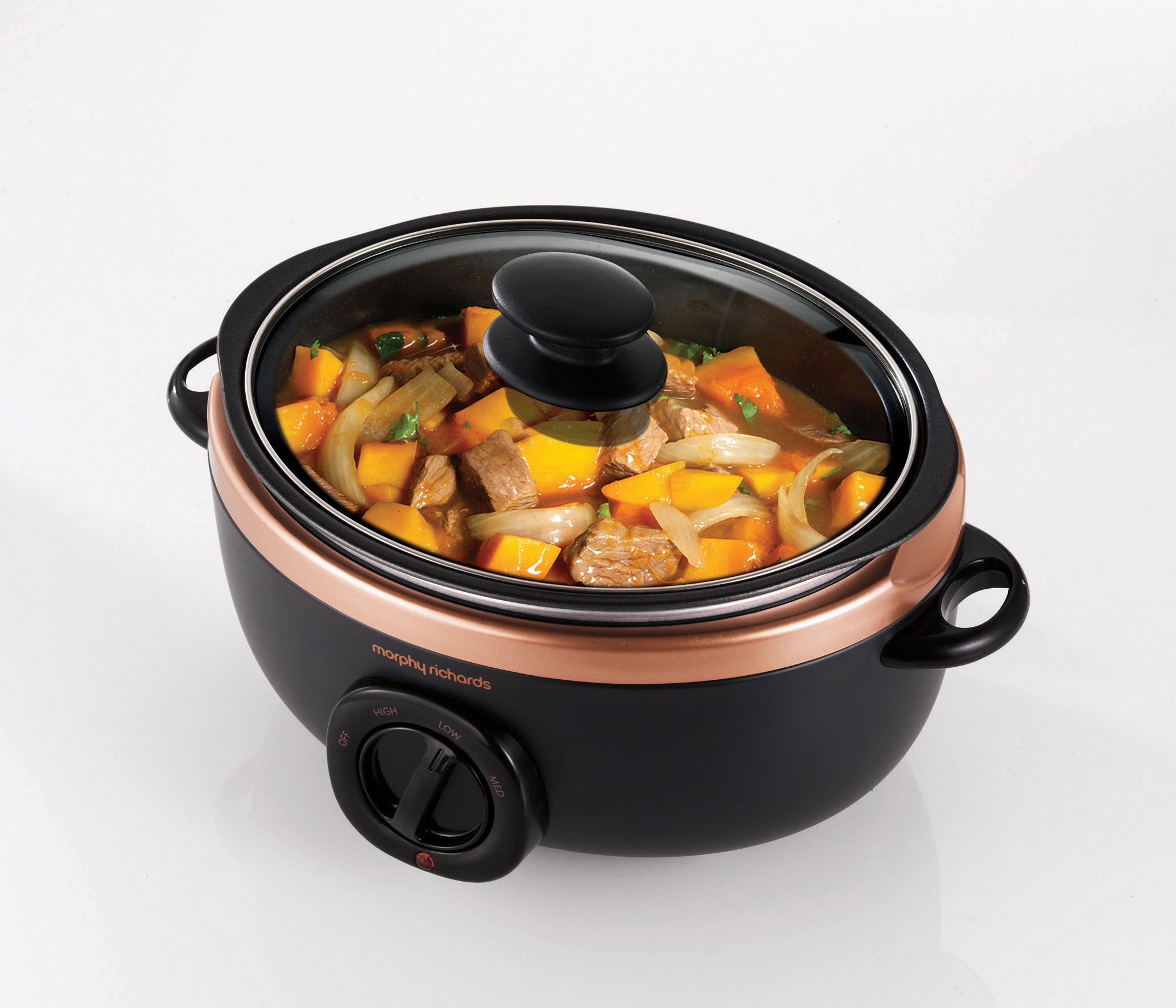 Ein schwarzer Slow Cooker mit Glasdeckel, gefüllt mit Eintopf und Gemüse. Kupferverkleidung.