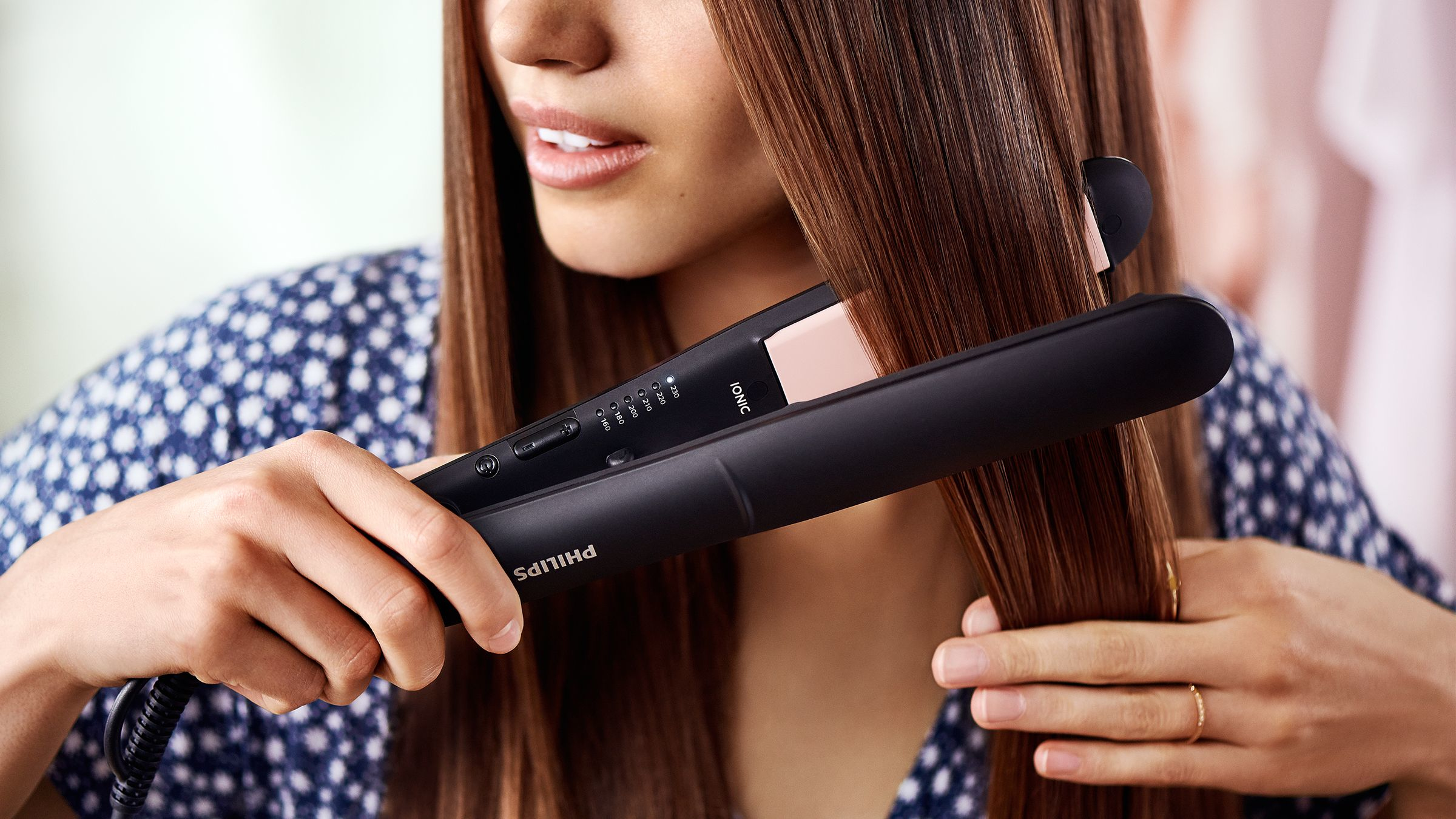Femme utilisant un lisseur noir sur des cheveux bruns. Gros plan.