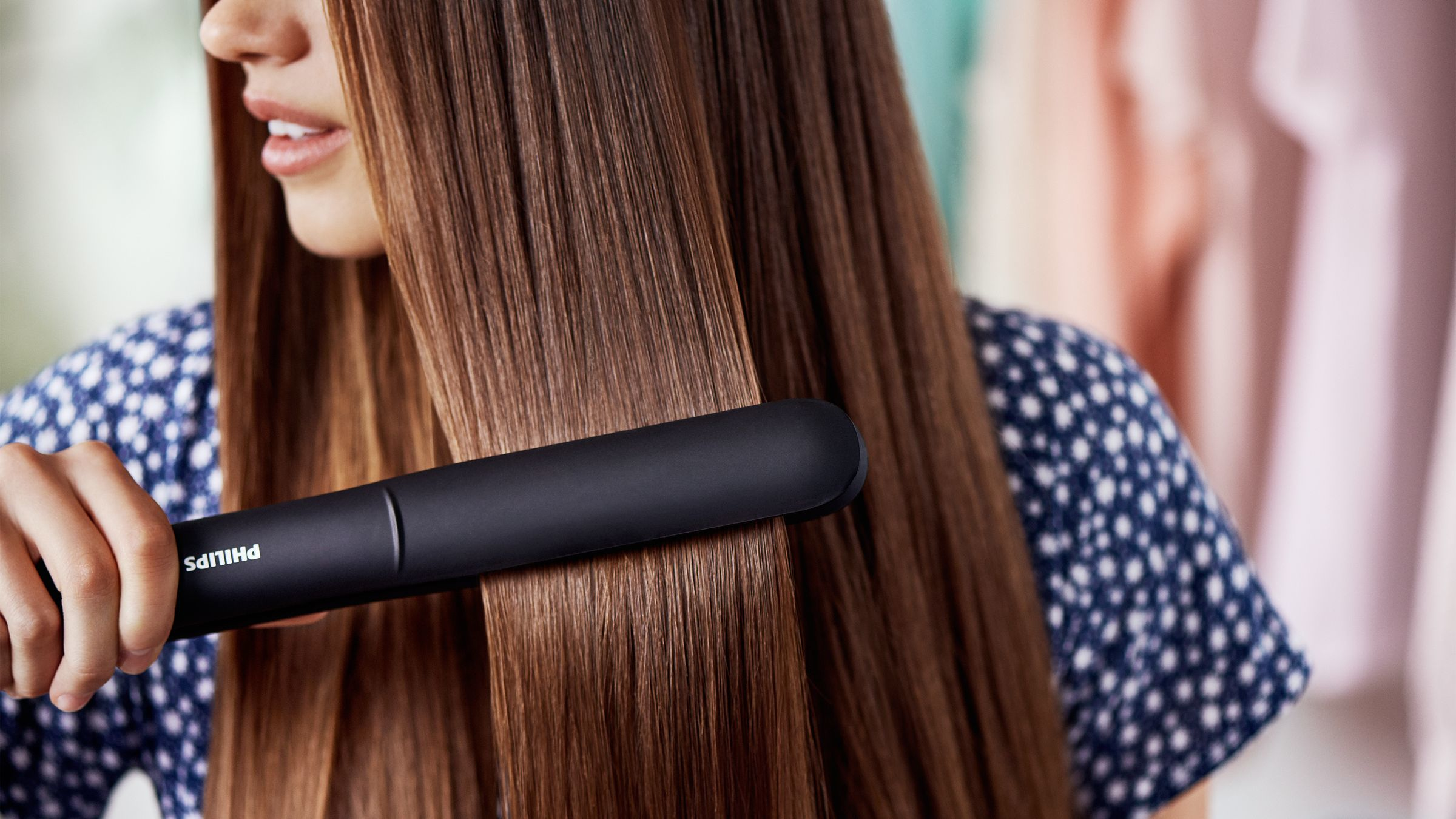 Femme se lissant les cheveux avec un lisseur Philips noir, gros plan.