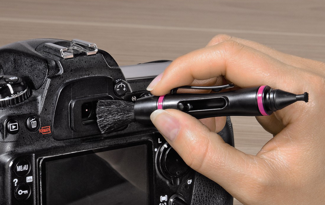Une main nettoyant l'objectif d'un appareil photo avec une brosse.