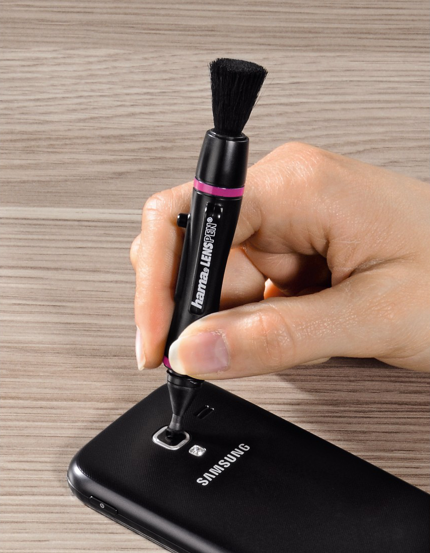 La main d'une personne tenant un outil de nettoyage noir près d'un téléphone.