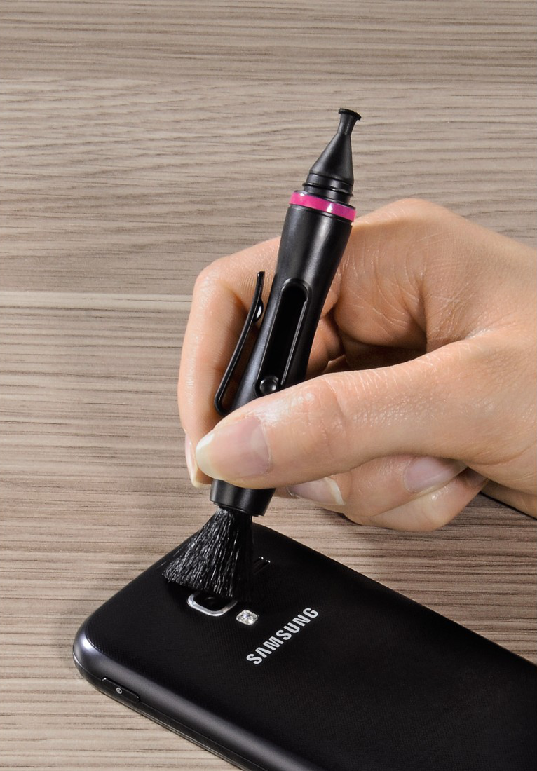 Main tenant une brosse de nettoyage noire au-dessus d'un téléphone noir.