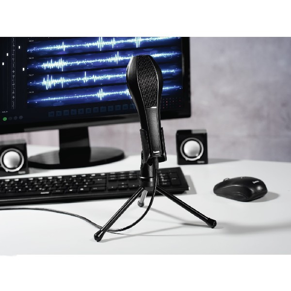 Micrófono negro en un soporte pequeño, colocado frente a un monitor de computadora.