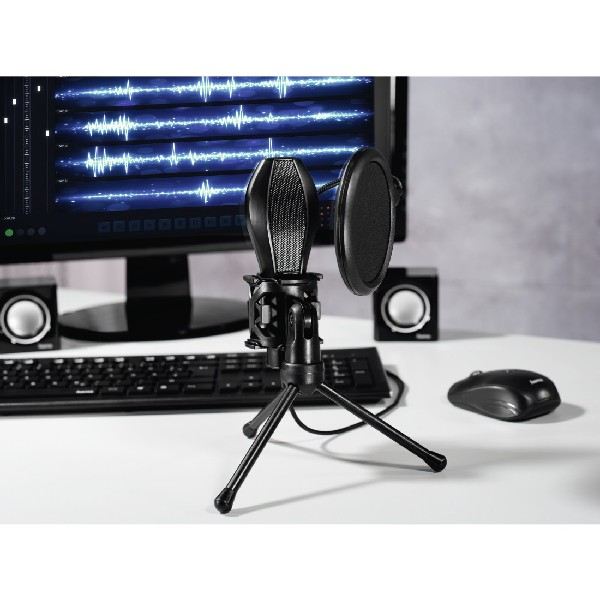 Un micrófono negro sobre un trípode, filtro antipop y altavoces sobre una mesa blanca, cerca de un teclado y un ratón.