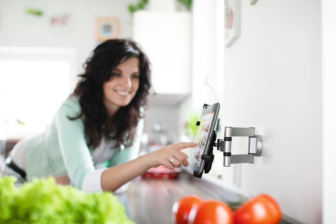 Femme touchant une tablette murale de cuisine. Tomates et laitue au premier plan.