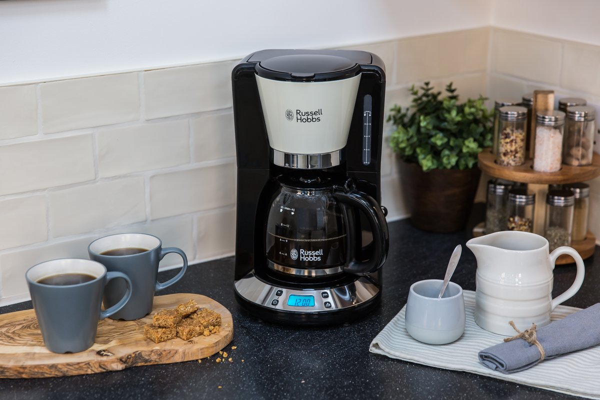 Coffee maker with a glass carafe, two mugs with coffee, some cookies, and spices.