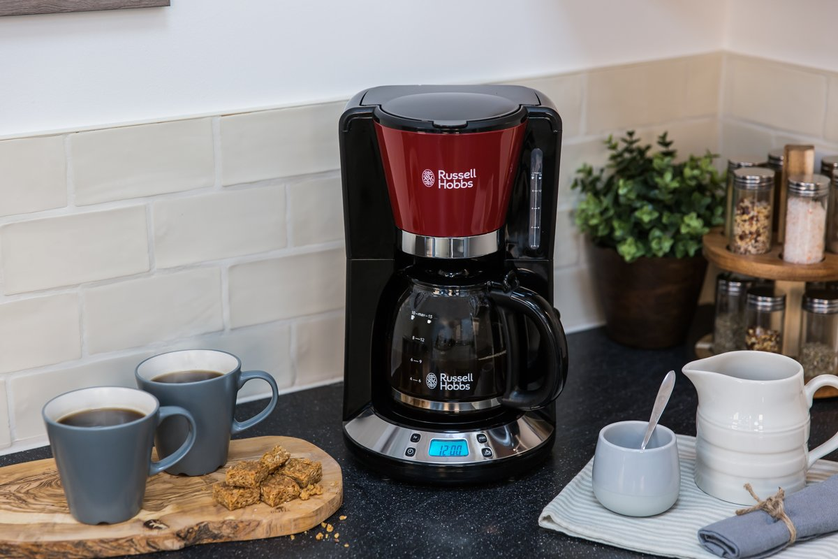 Coffee maker on a counter with cups and a cutting board with cookies.