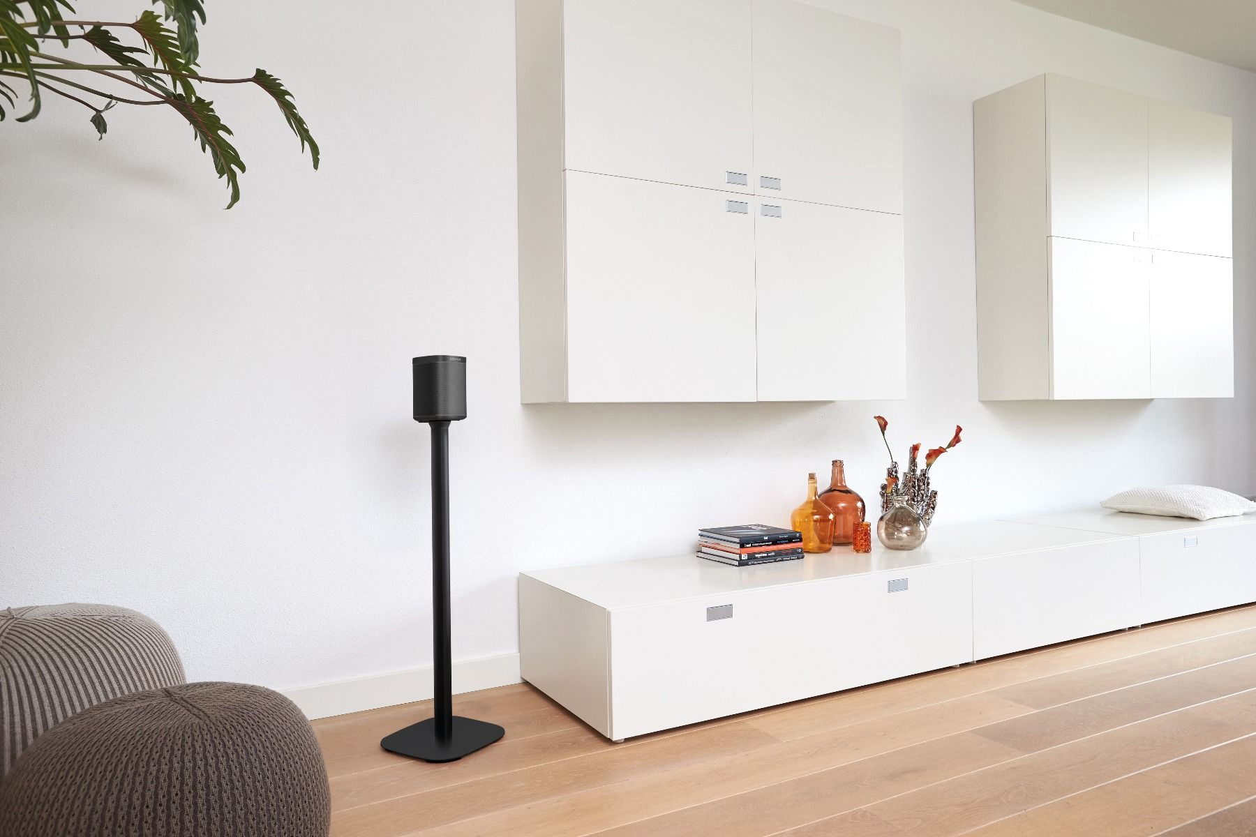Modernes Wohnzimmer mit weißen Schränken und einem schwarzen Lautsprecher auf einem Ständer. Holzfußboden.