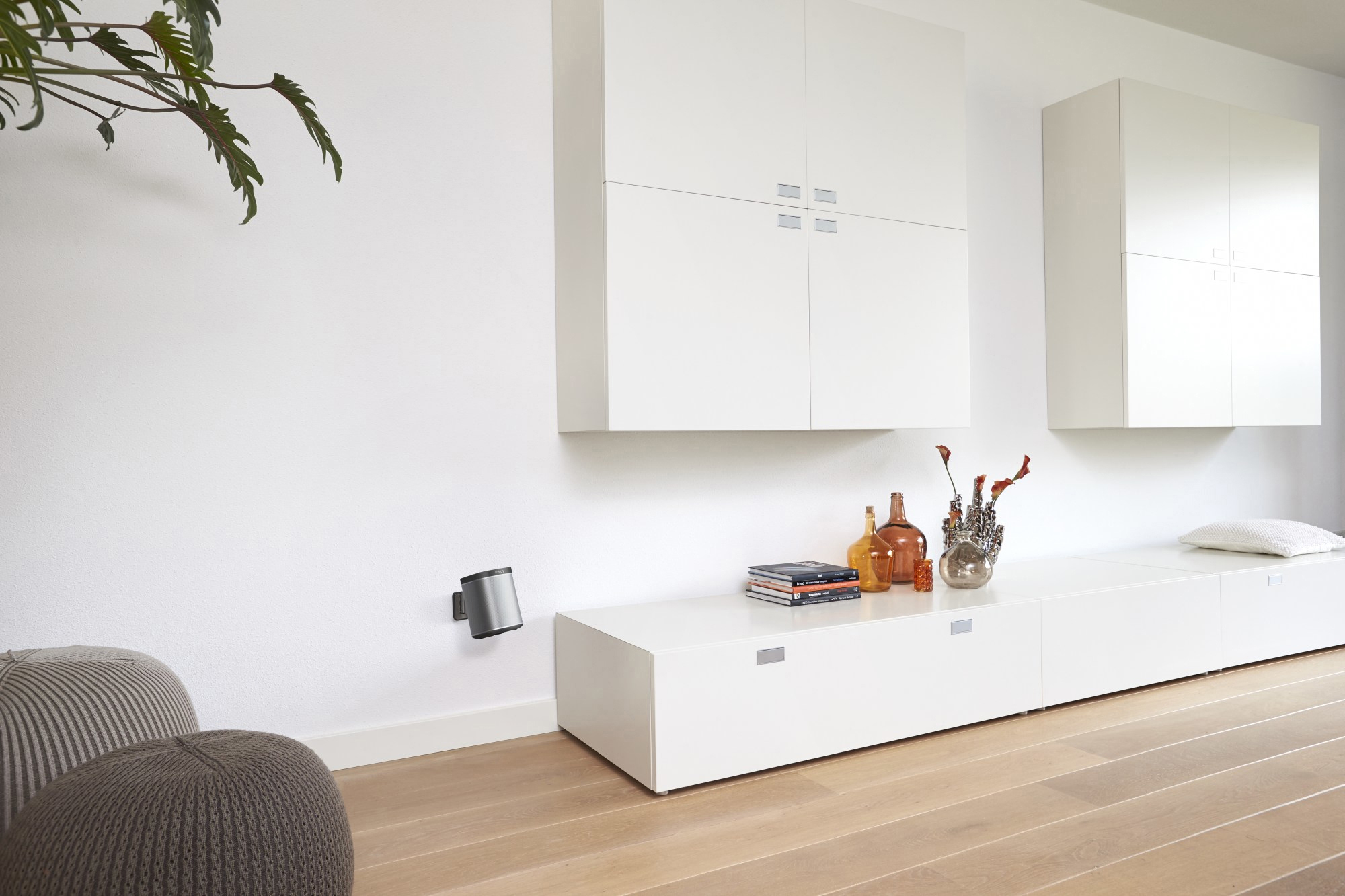 Modernes Wohnzimmer mit weißen Wänden, weißen Schränken, Holzboden und Dekoration. Ein Wandlautsprecher ist sichtbar.