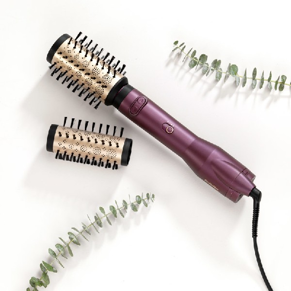 Un cepillo de peinado morado con dos cabezales intercambiables y decoración de hojas verdes.