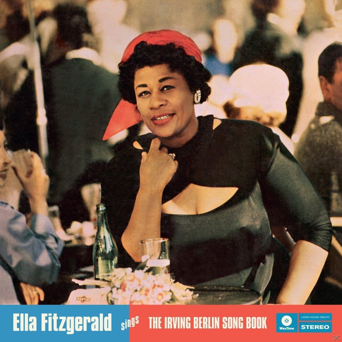Ella Fitzgerald vörös fejkendővel és fekete felsőben ül egy étteremben, előtte üveg és virágok.