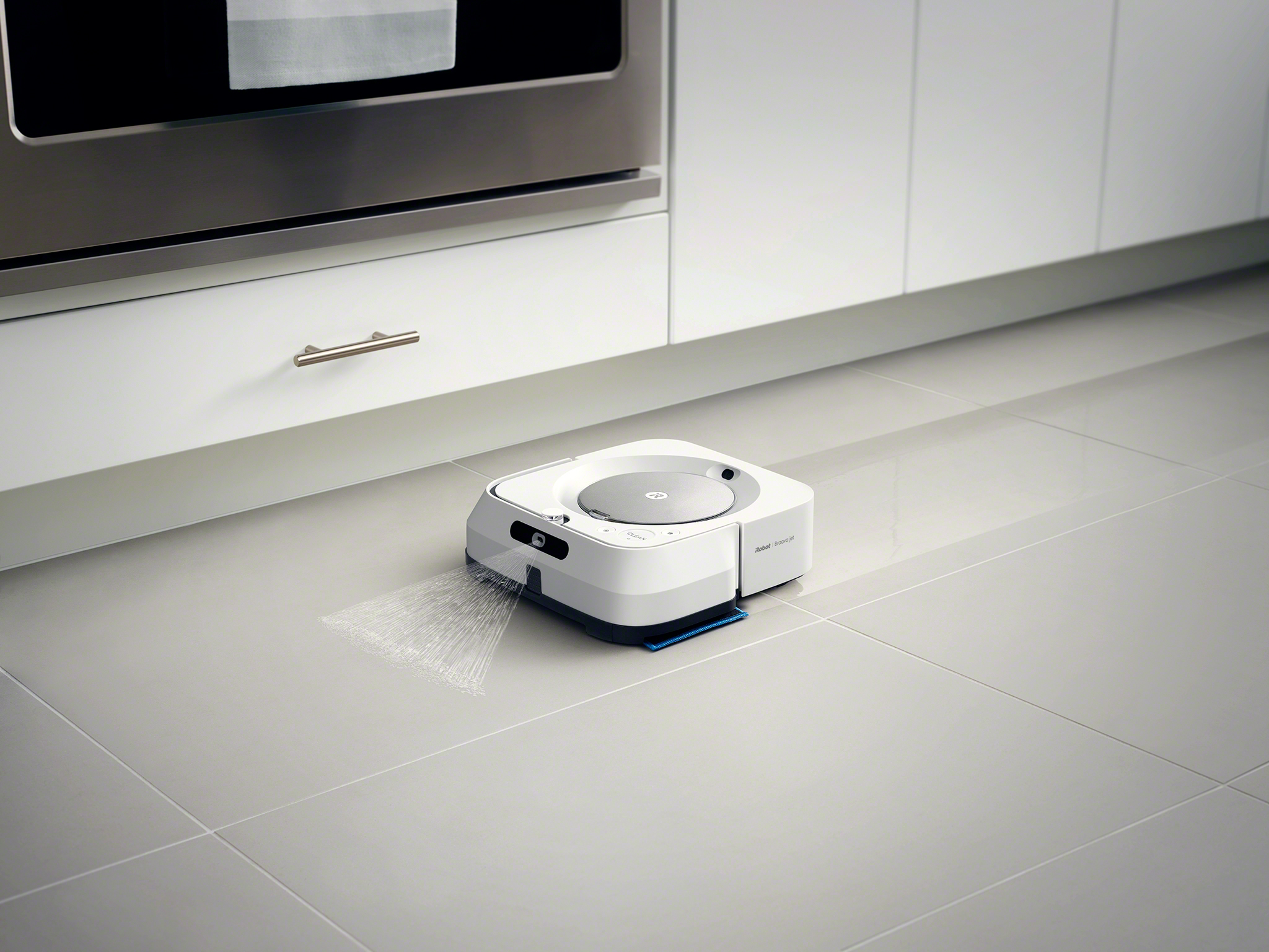 A white robot vacuum cleaner cleans a kitchen floor.