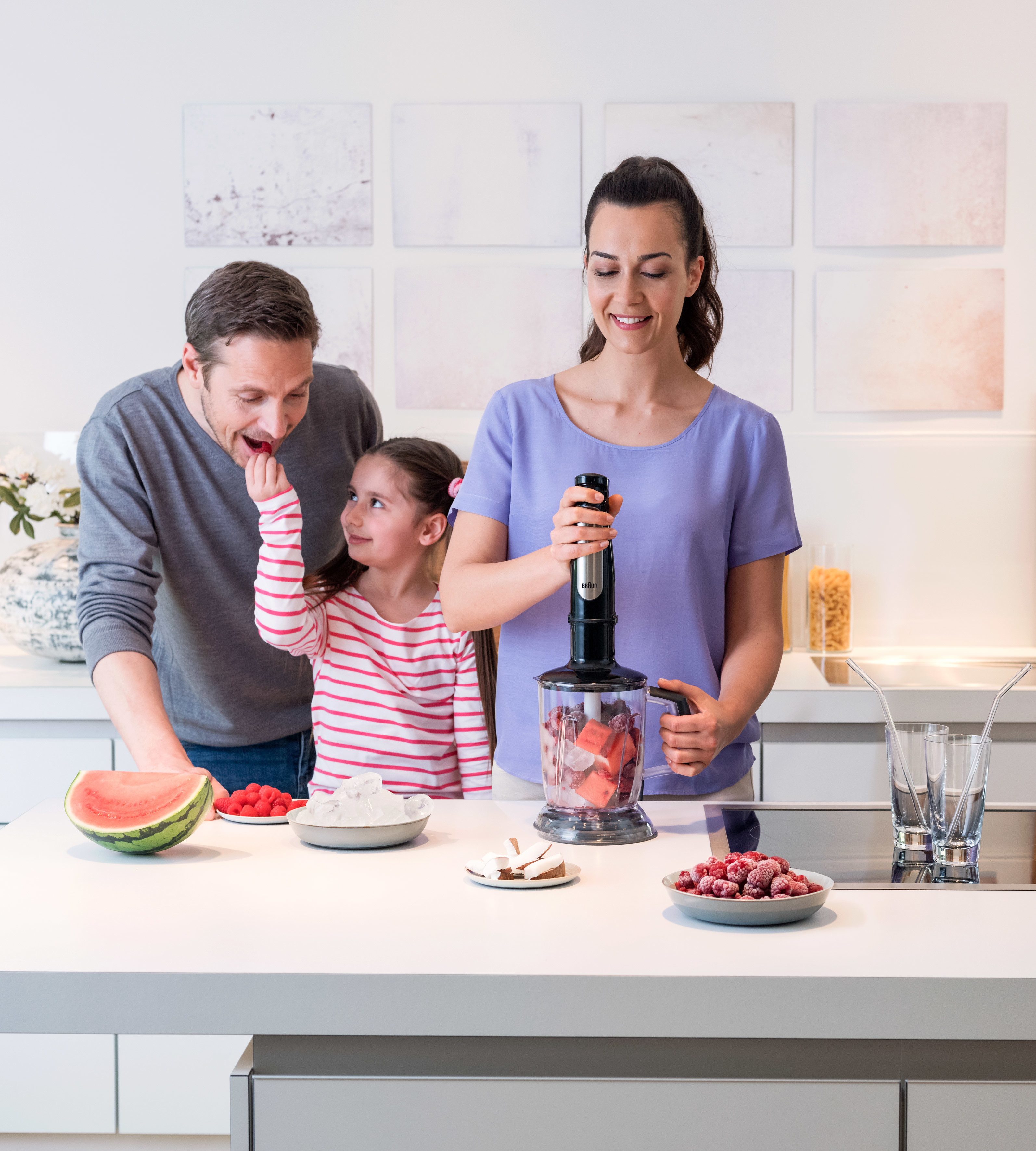 Familie macht einen Smoothie. Ein Mann, ein Mädchen und eine Frau sind in der Küche. Sie benutzen einen Mixer.