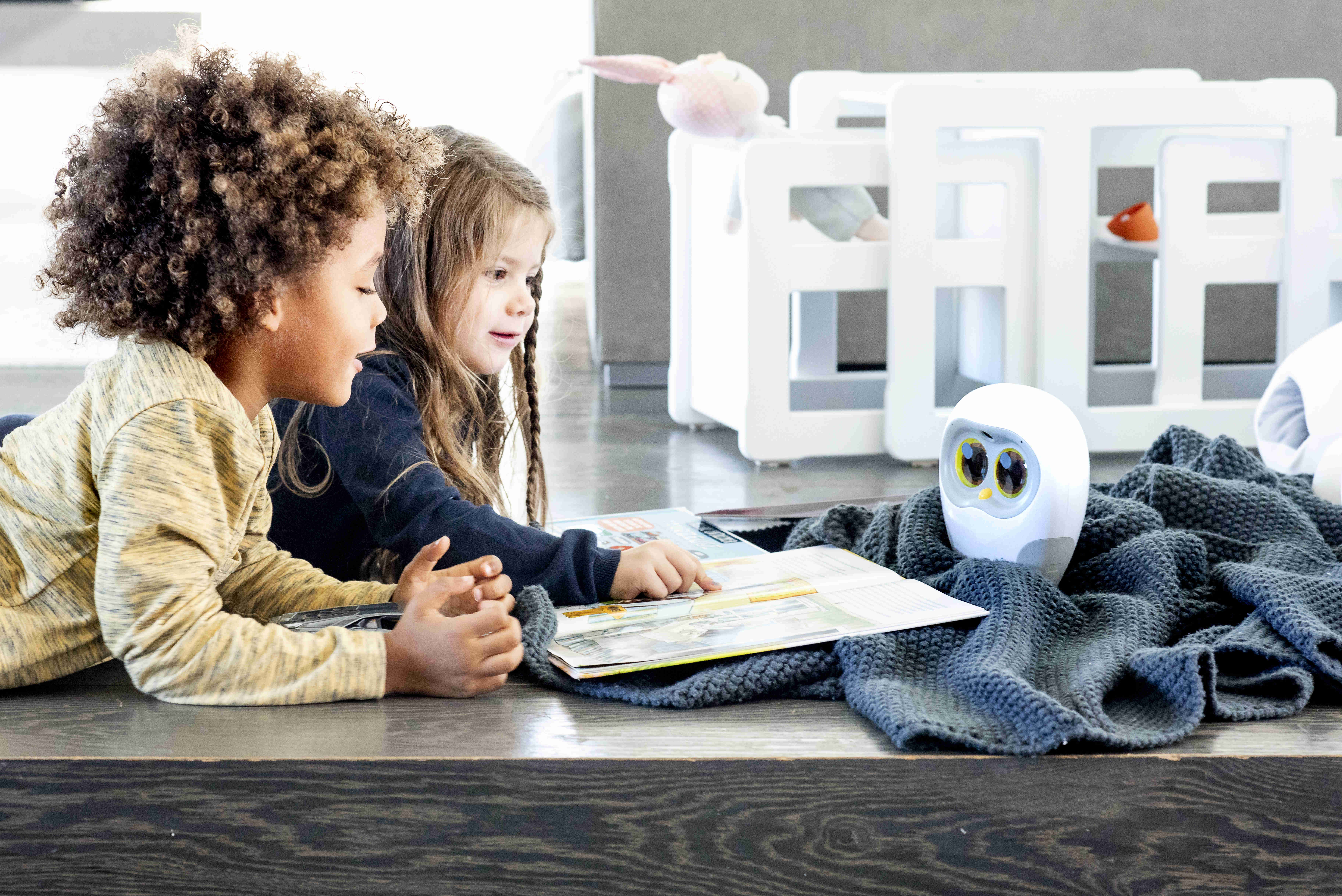 Zwei Kinder und ein Roboter lesen ein Buch in der Nähe eines Kinderbettes.