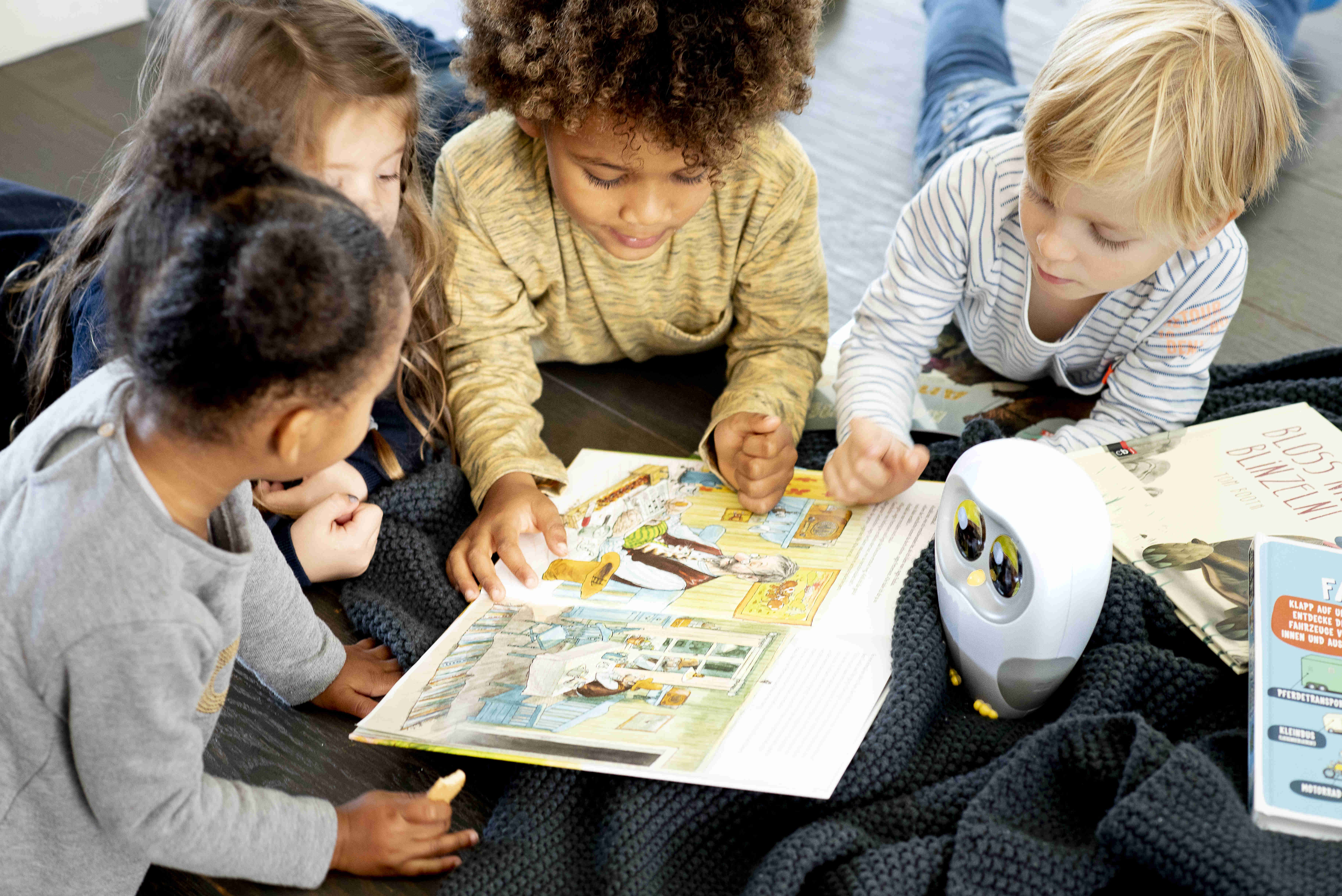 Kinder lesen gemeinsam ein Buch, mit Roboter-Eule und Büchern auf dunkler Decke.