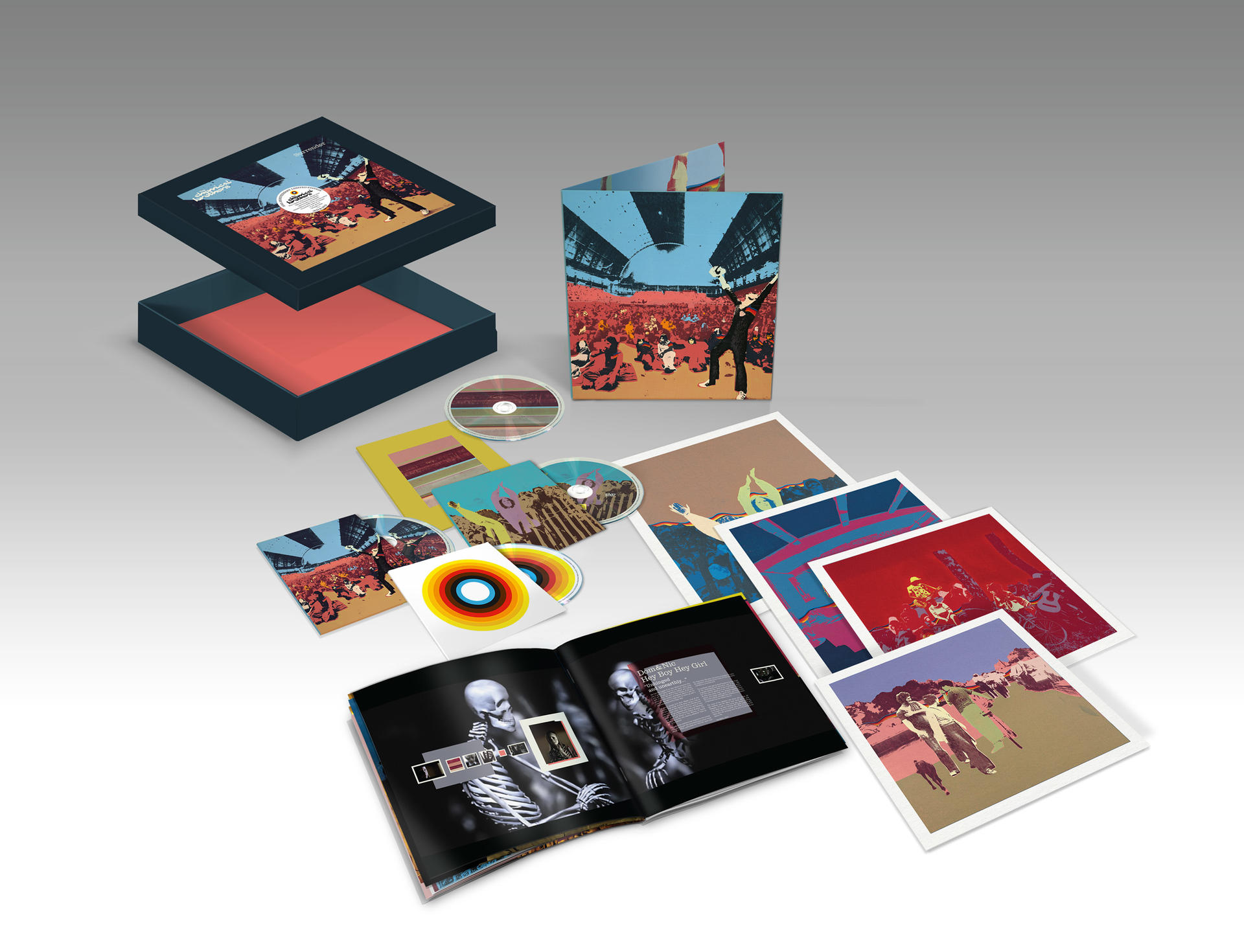 Een open boxset met een deksel met een concertscène. Cd's, boekjes en kunstprints zijn verspreid, allemaal met artistieke ontwerpen.