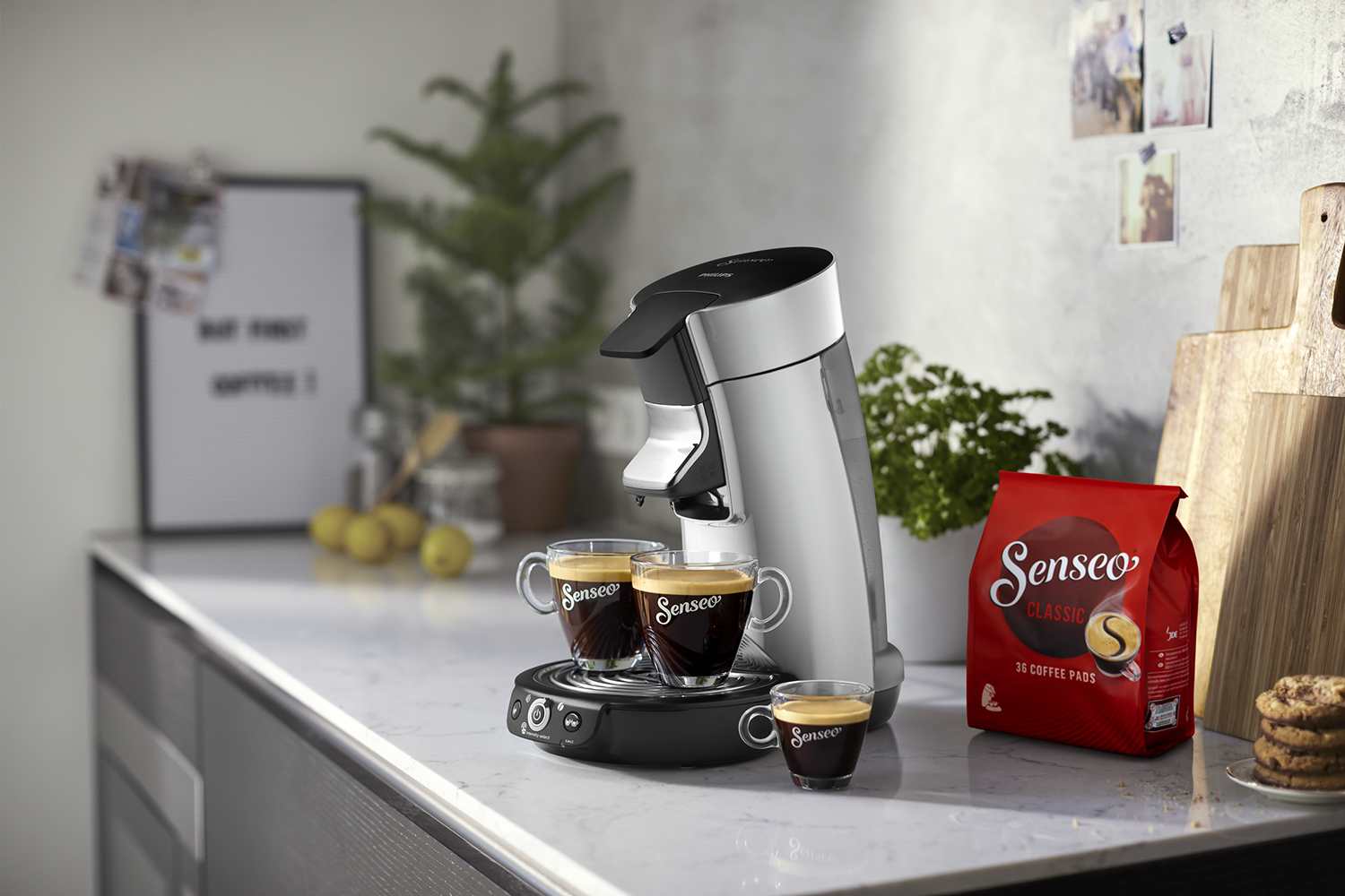 Koffiezetapparaat met twee kopjes koffie, koffiepads en koekjes.