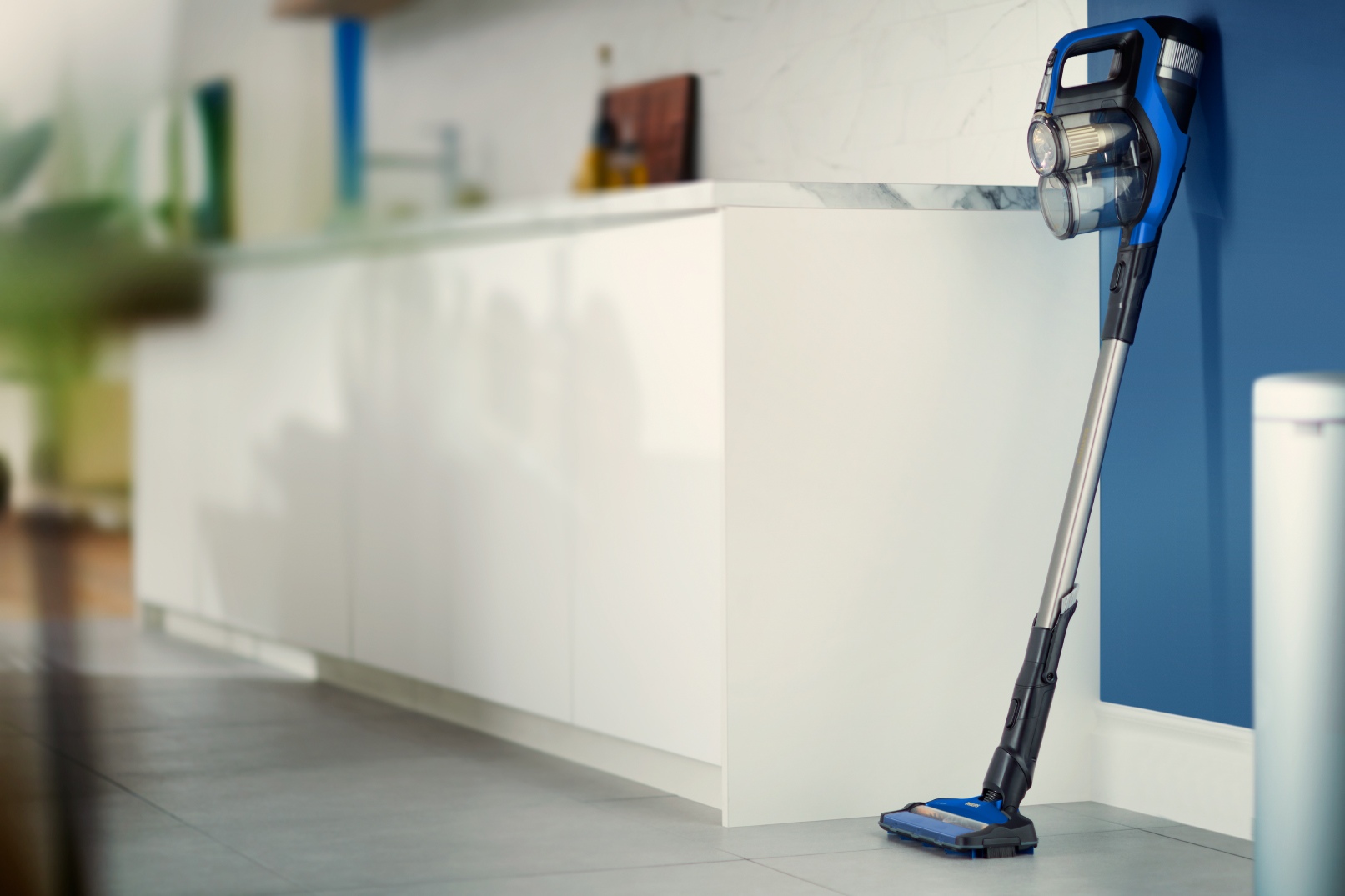 Een blauwe en zwarte stofzuiger staat tegen een blauwe muur in een moderne keuken.