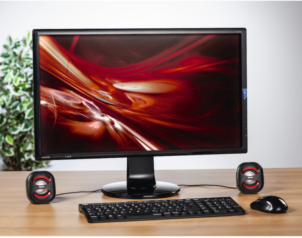 Configuration informatique avec moniteur, haut-parleurs, clavier et souris sur un bureau en bois. Thème rouge et noir.