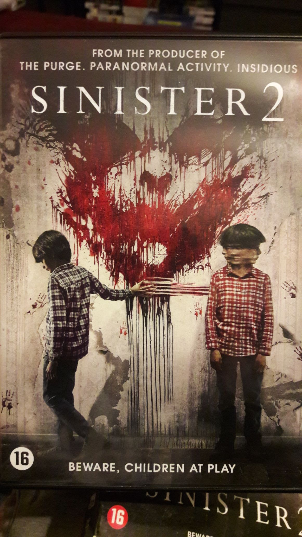 Pochette de film : Sinister 2. Deux garçons, du sang et un contour de visage effrayant sur un mur.