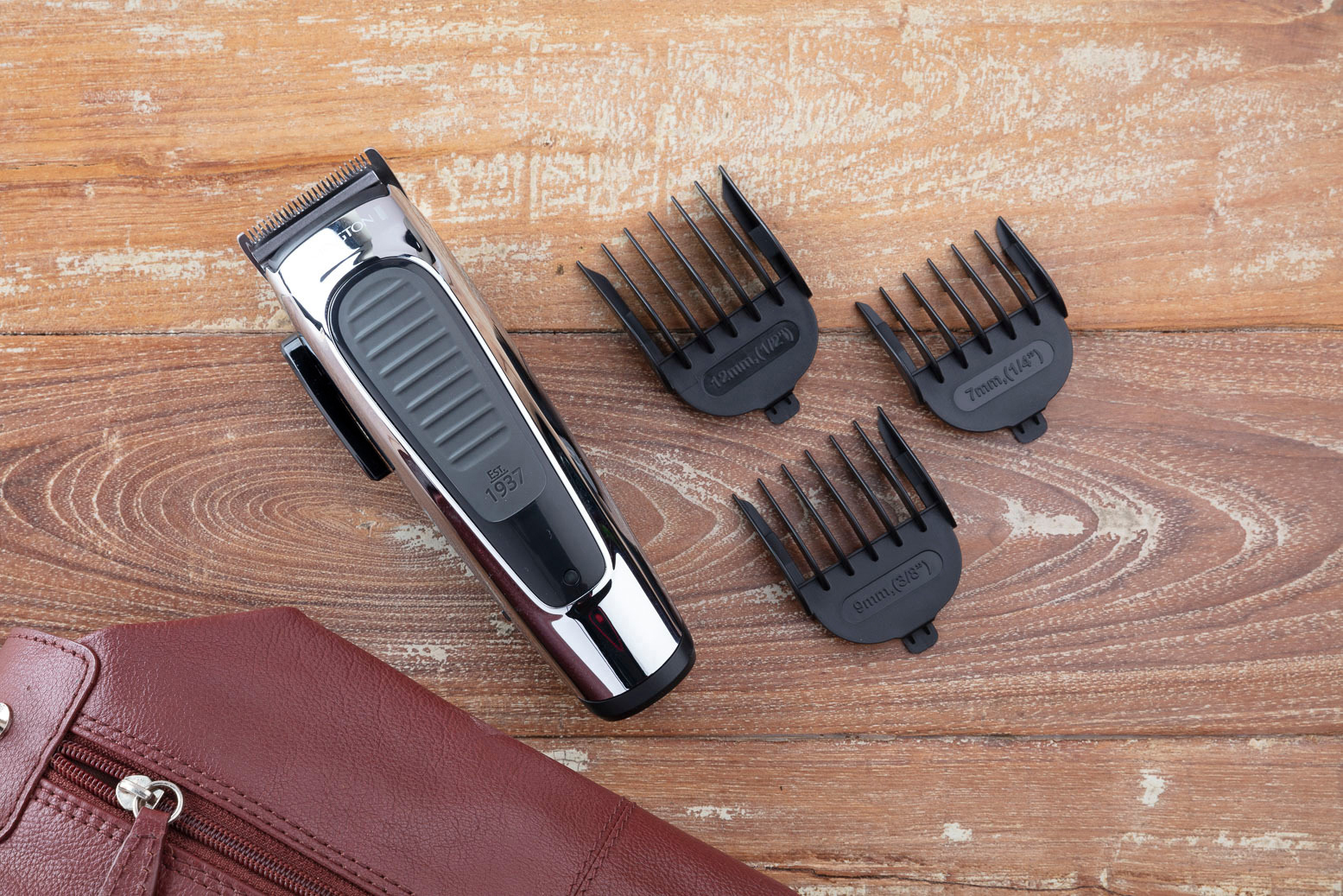 Haarschneider mit Aufsatzkämmen. Auf Holzoberfläche mit brauner Tasche platziert.