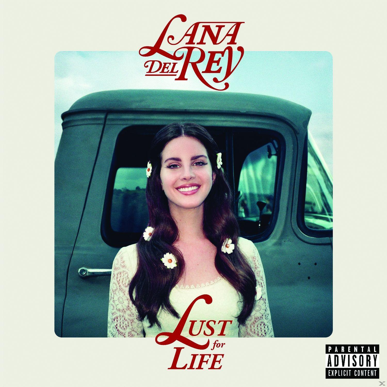 Pochette d'album de Lana Del Rey, souriante avec des fleurs dans les cheveux, devant un camion.