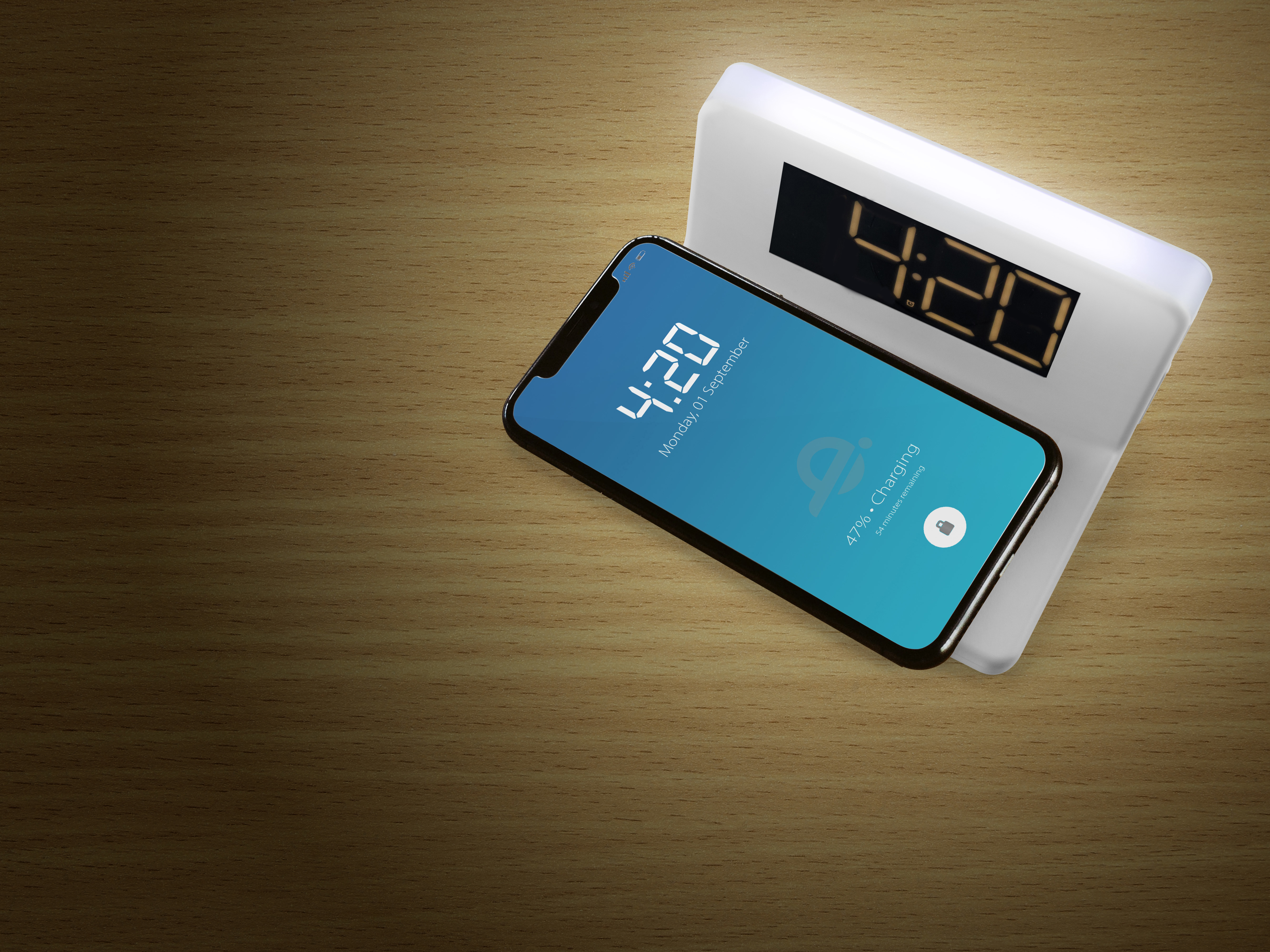 Eine weiße Uhr, die ein Telefon auflädt. Die Uhrzeit ist 4:20. Das Telefon zeigt das Datum.