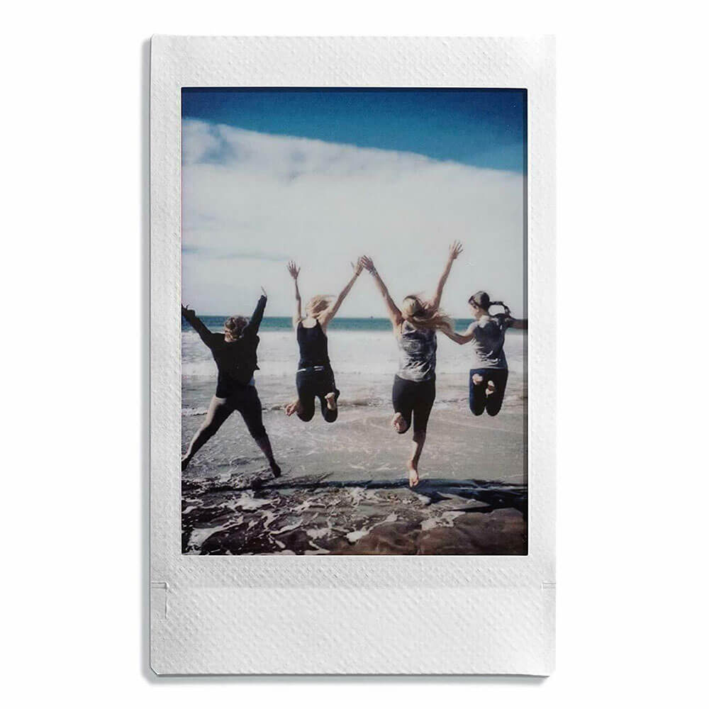Polaroid photo of four people jumping on a beach, arms raised. Blue sky and ocean.