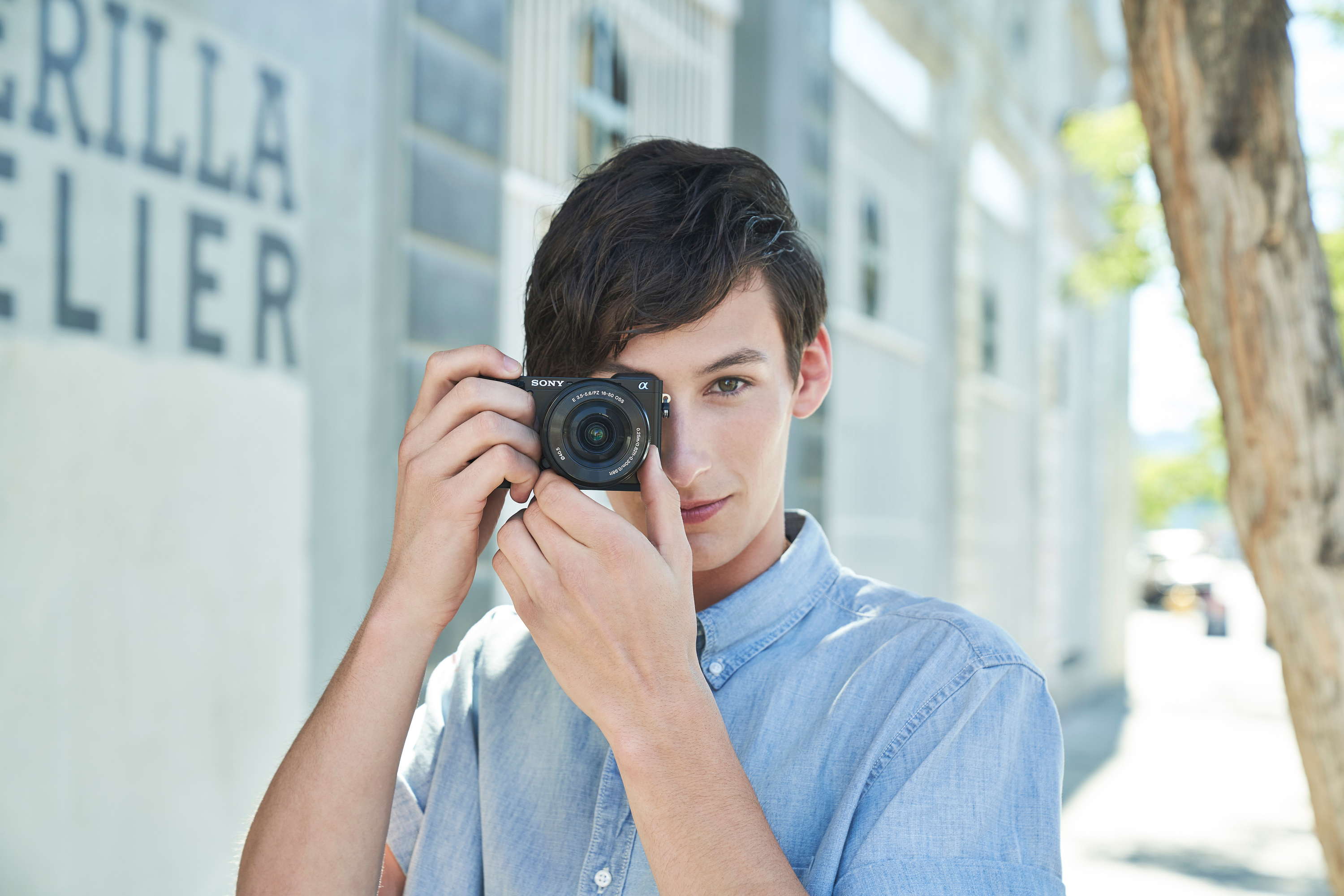 Young man holding a camera, smiling, near a building.